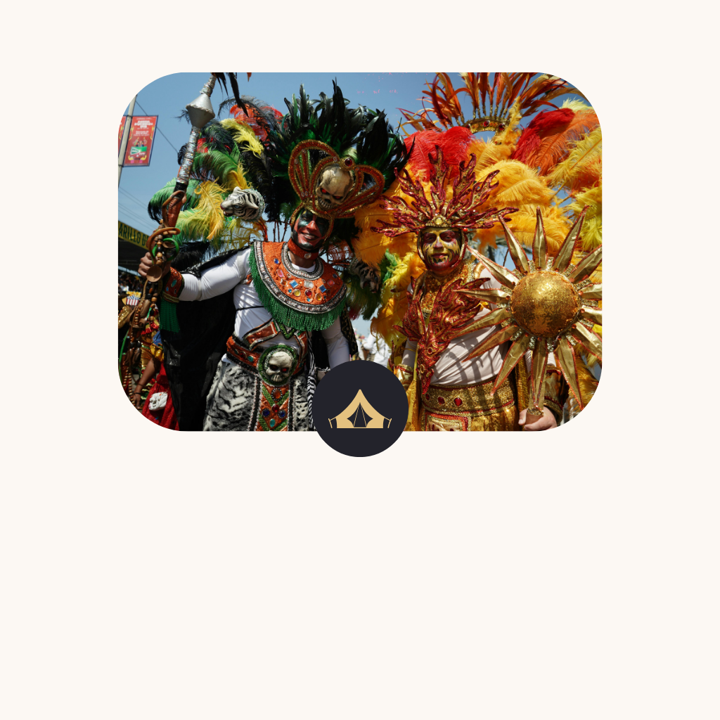 Two people dressed in colorful, elaborate costumes with feathers and metallic accents participate in a cultural parade or celebration.