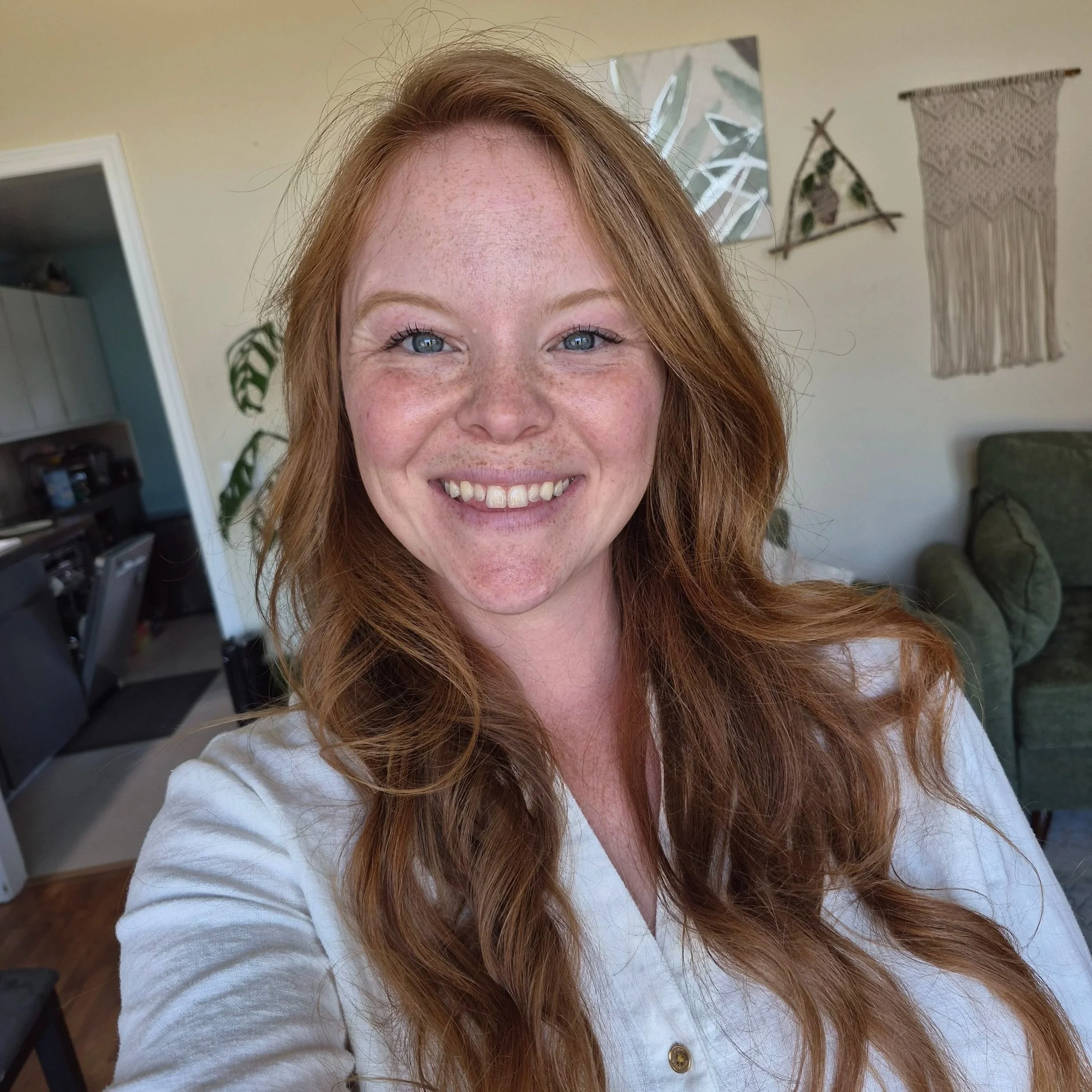 Close-up of a smiling woman with red hair, blue eyes, and freckles, wearing a white top, birth doula - postpartum doula - lactation counselor - birth educator.