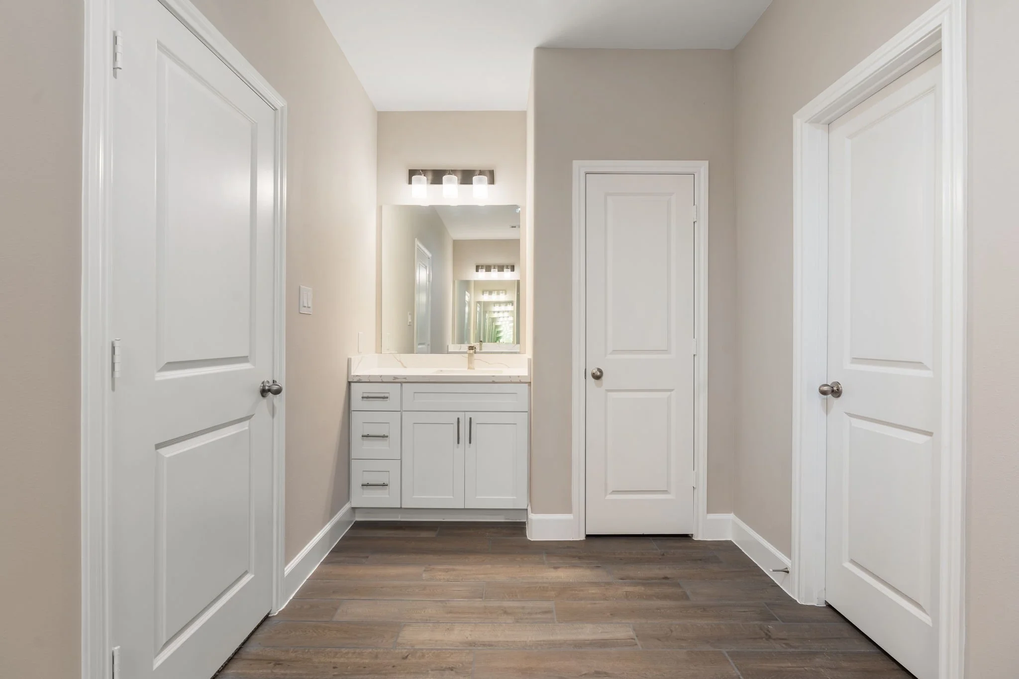 Bathroom with four white doors, a white vanity with a mirror, and wooden flooring.