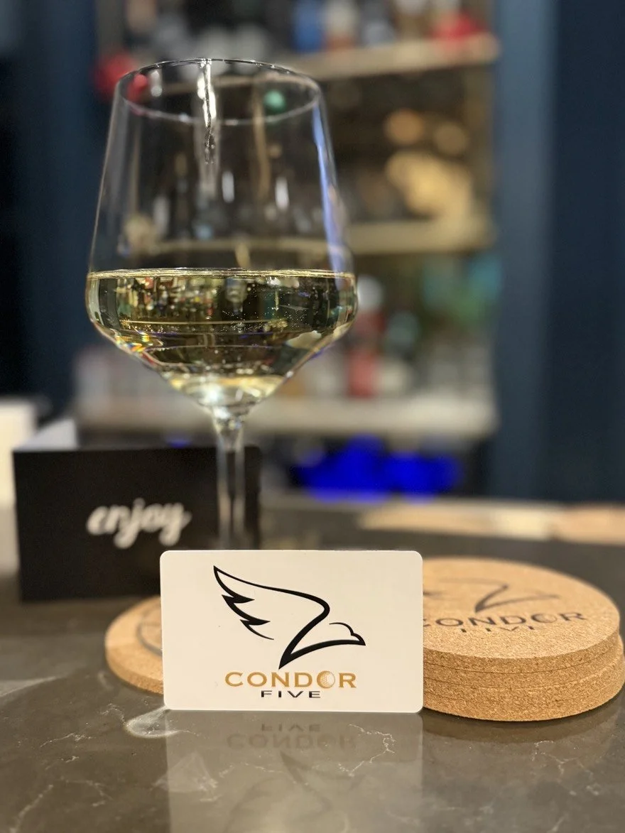 Modern bar with a marble countertop, nine yellow barstools, a blue wall with a mounted TV, glass shelves with liquor bottles, and hanging pendant lights.