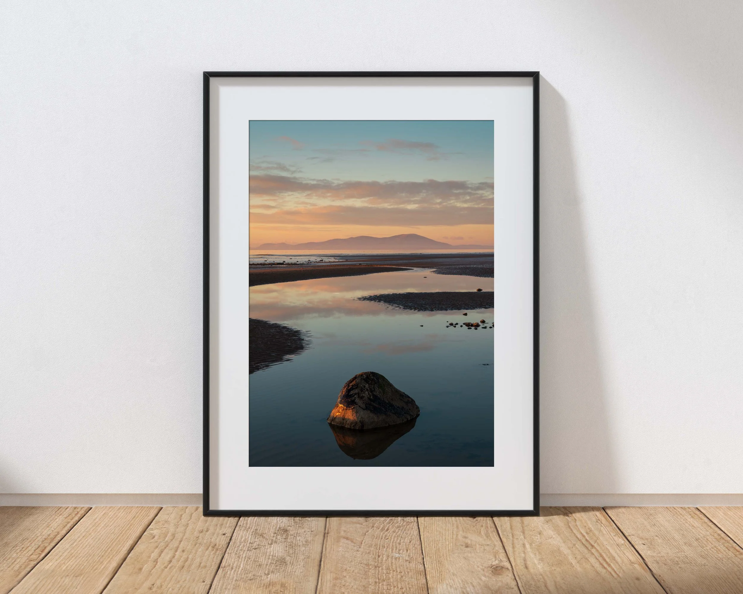 Framed landscape photograph of a beach with a large rock in the foreground and a mountain in the background at sunset.