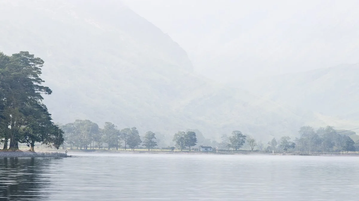 Calm lake with trees along the shoreline and a misty mountain in the background.