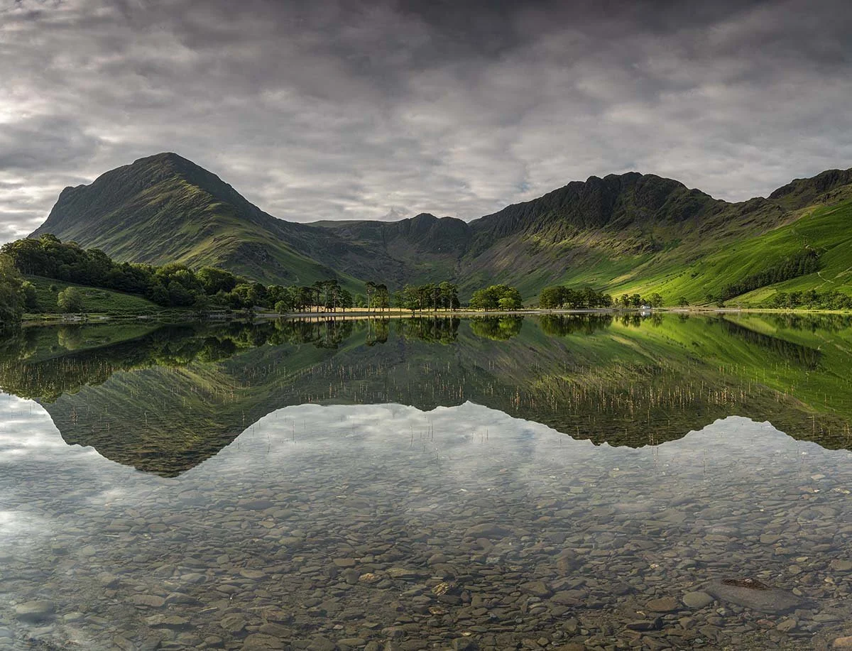 A calm lake Buttermere reflecting green mountains and cloudy sky.