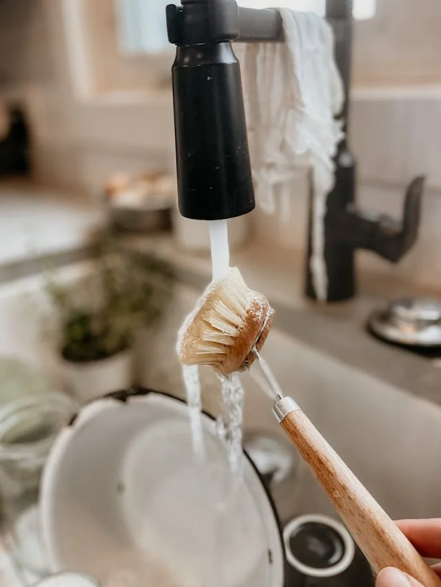 A sink faucet with a toothbrush hanging from it under running water in a kitchen.