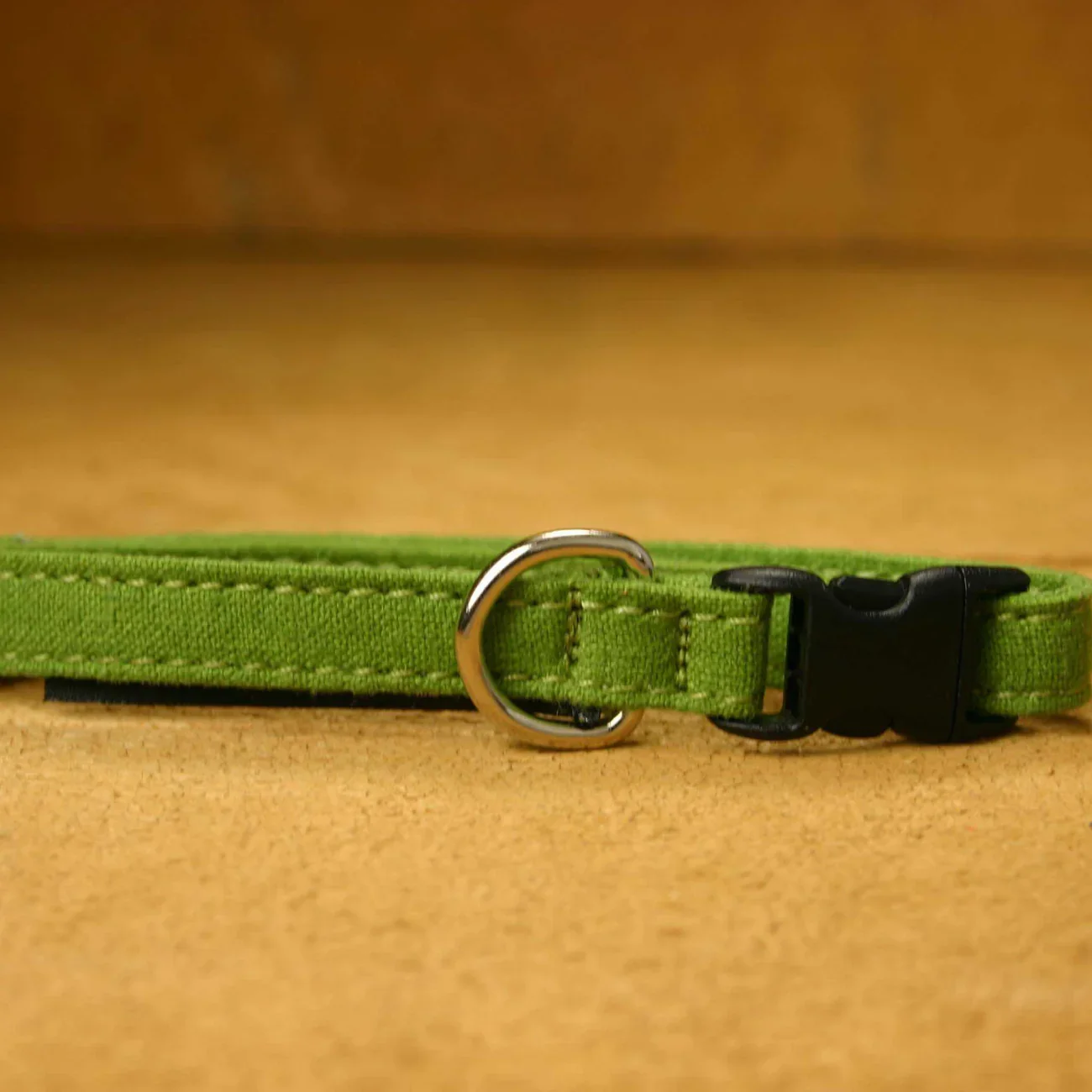 Close-up of a green fabric pet collar with a silver metal D-ring and a black plastic buckle, placed on a wooden surface.
