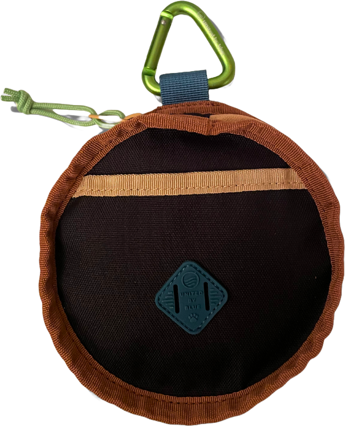 Close-up of a circular black and brown pet accessory with a green carabiner and a small blue tag, used for attaching or carrying items.