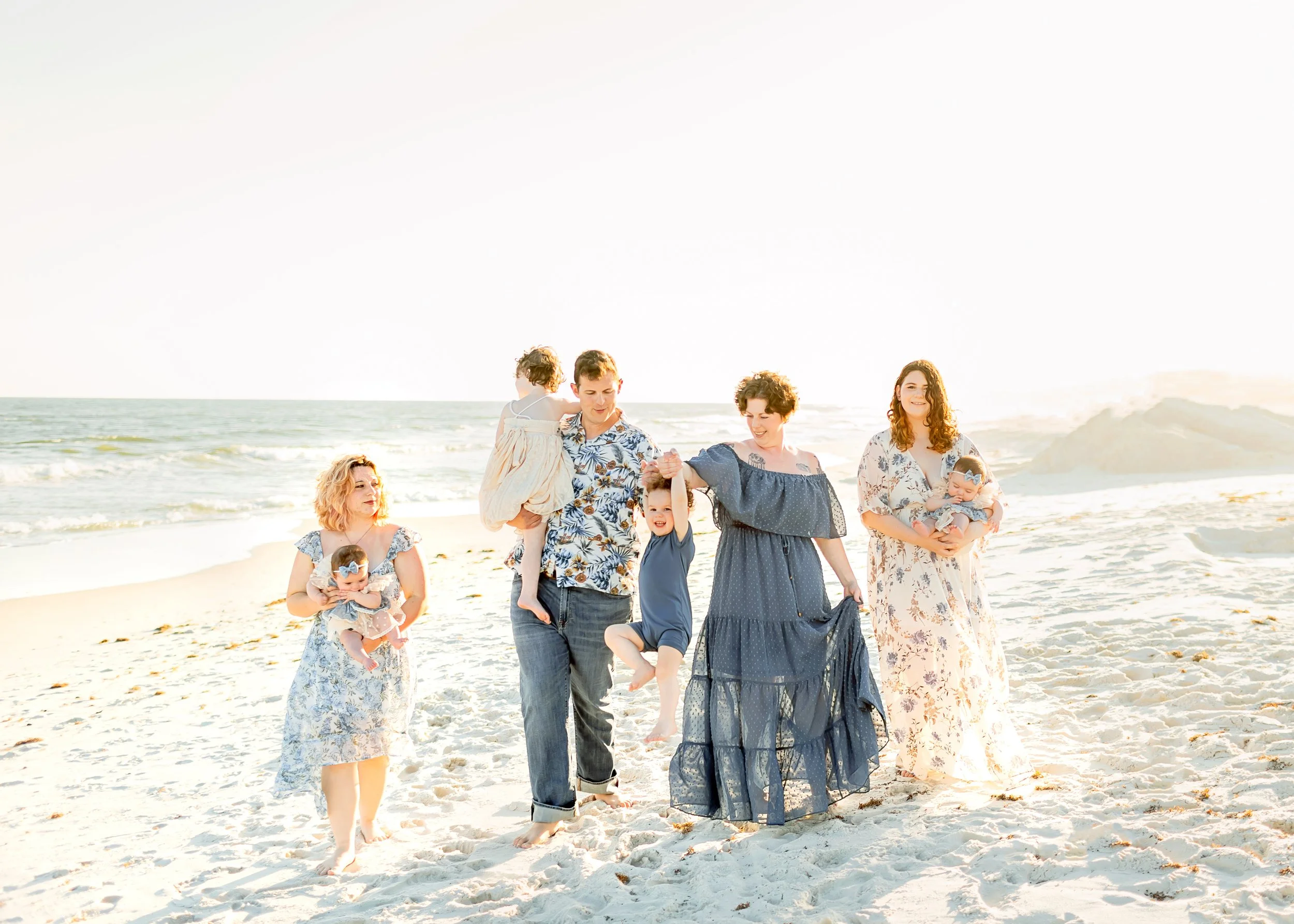 Family walking on the beach during sunset, carrying young children, some holding hands, enjoying a sunny day.