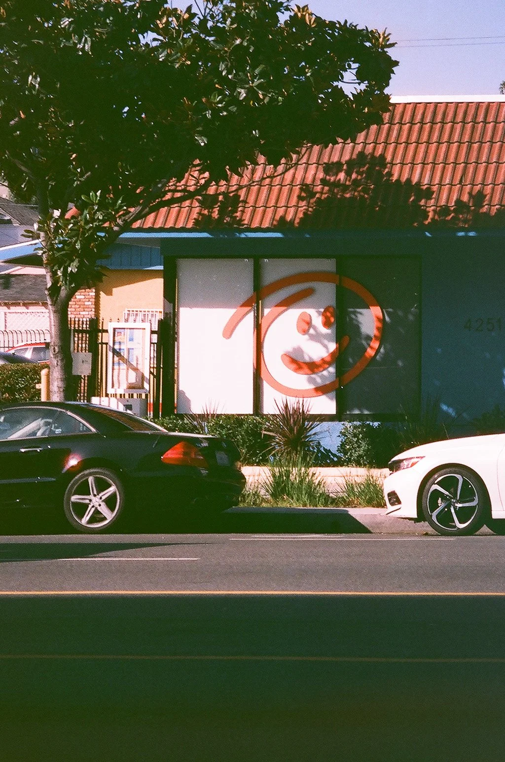 A building with a large smiley face on the front window, parked cars in front, a tree to the left, and clear sky above.