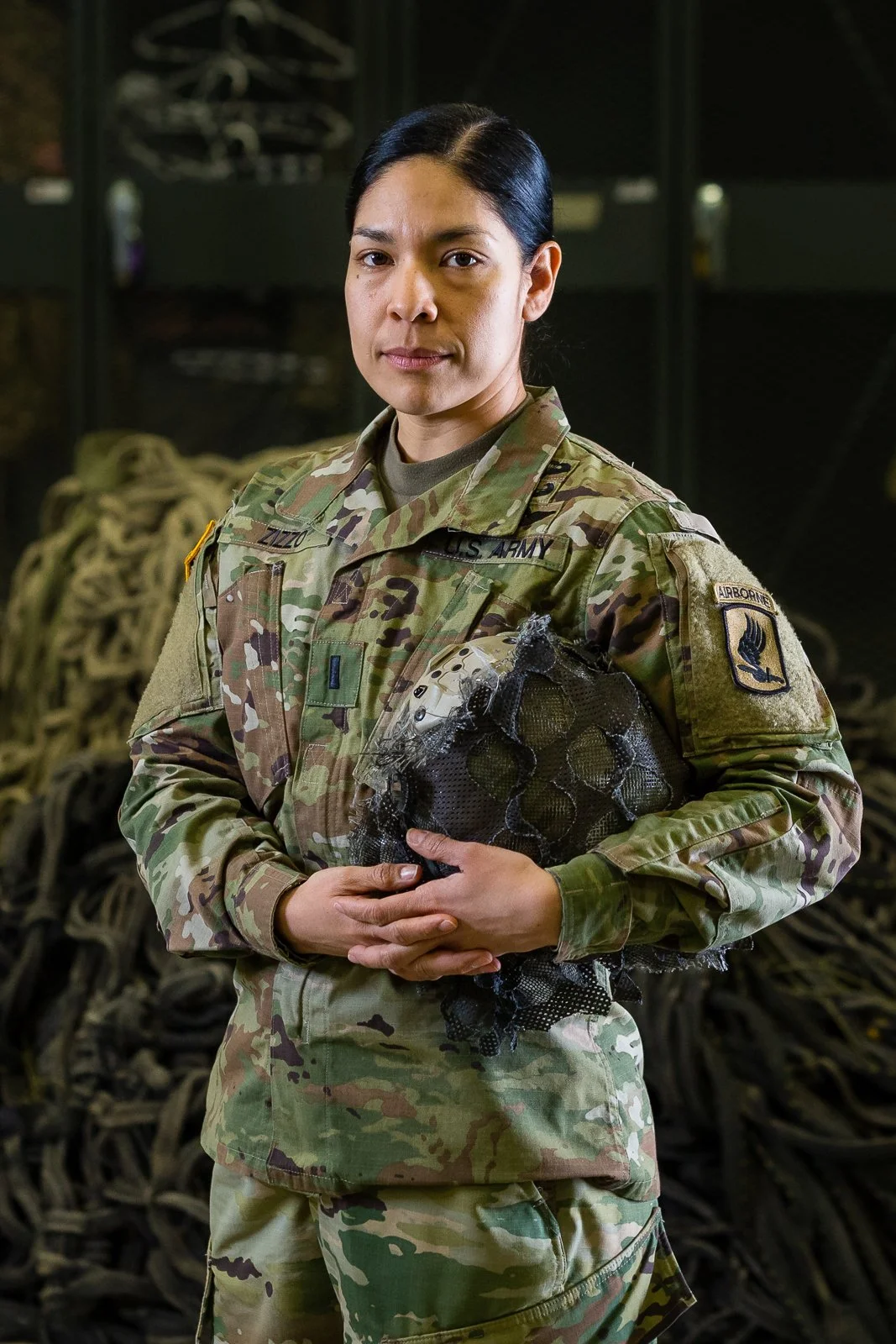 A female soldier in camouflage uniform holding a helmet inside a military setting.