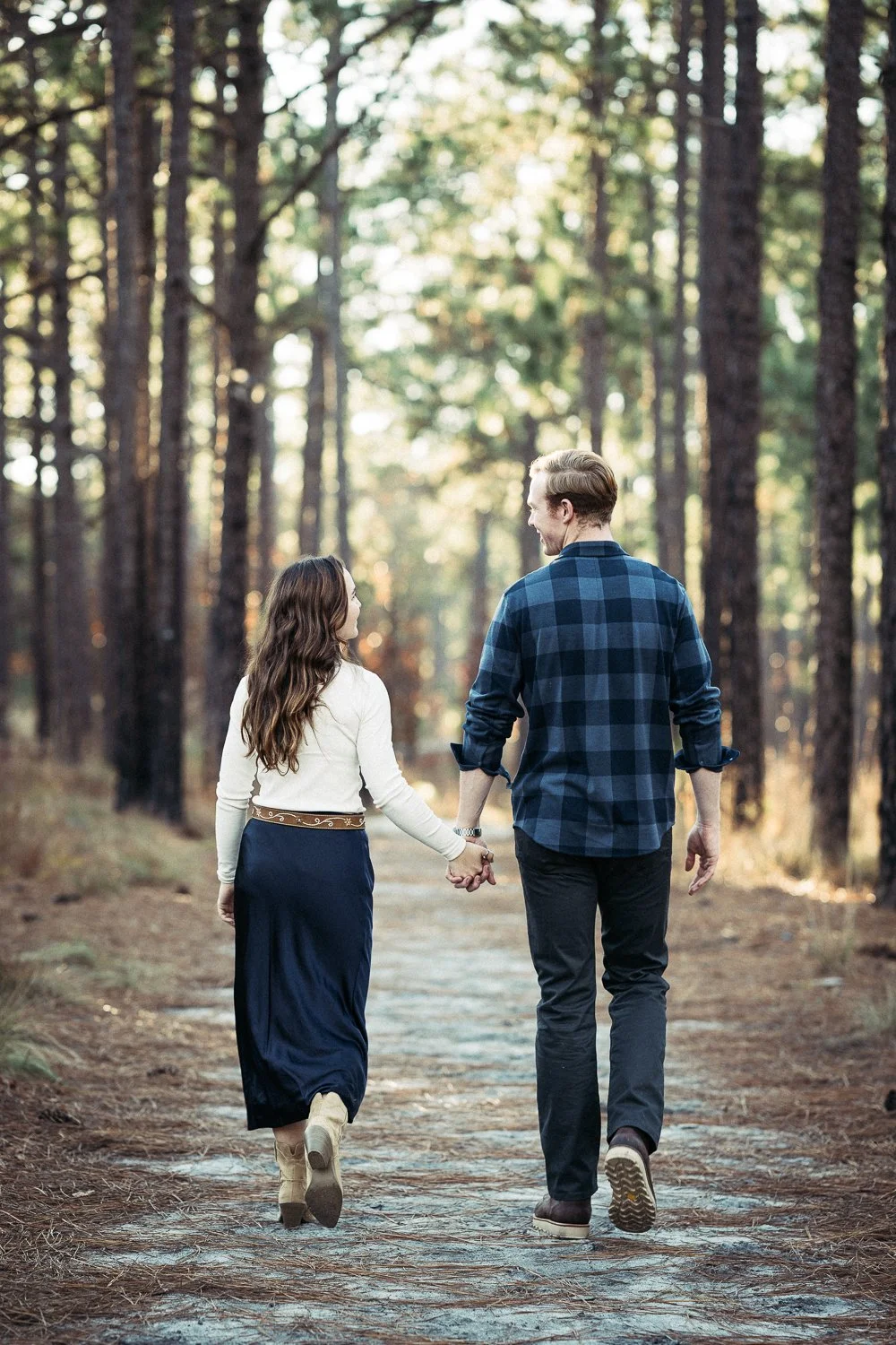 A couple holding hands and walking down a trail in a forest.