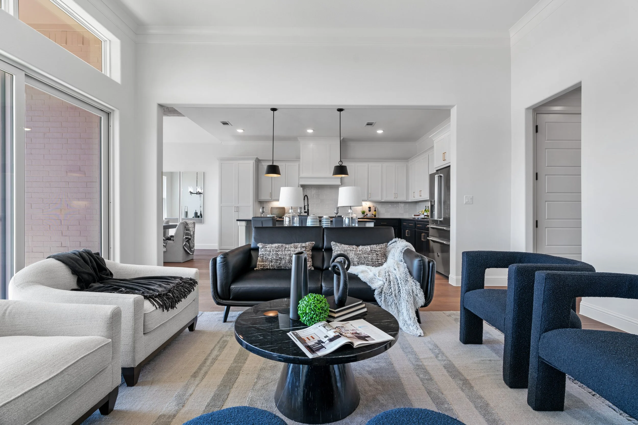 Living room with white and navy furniture, black coffee table, and open kitchen in background.