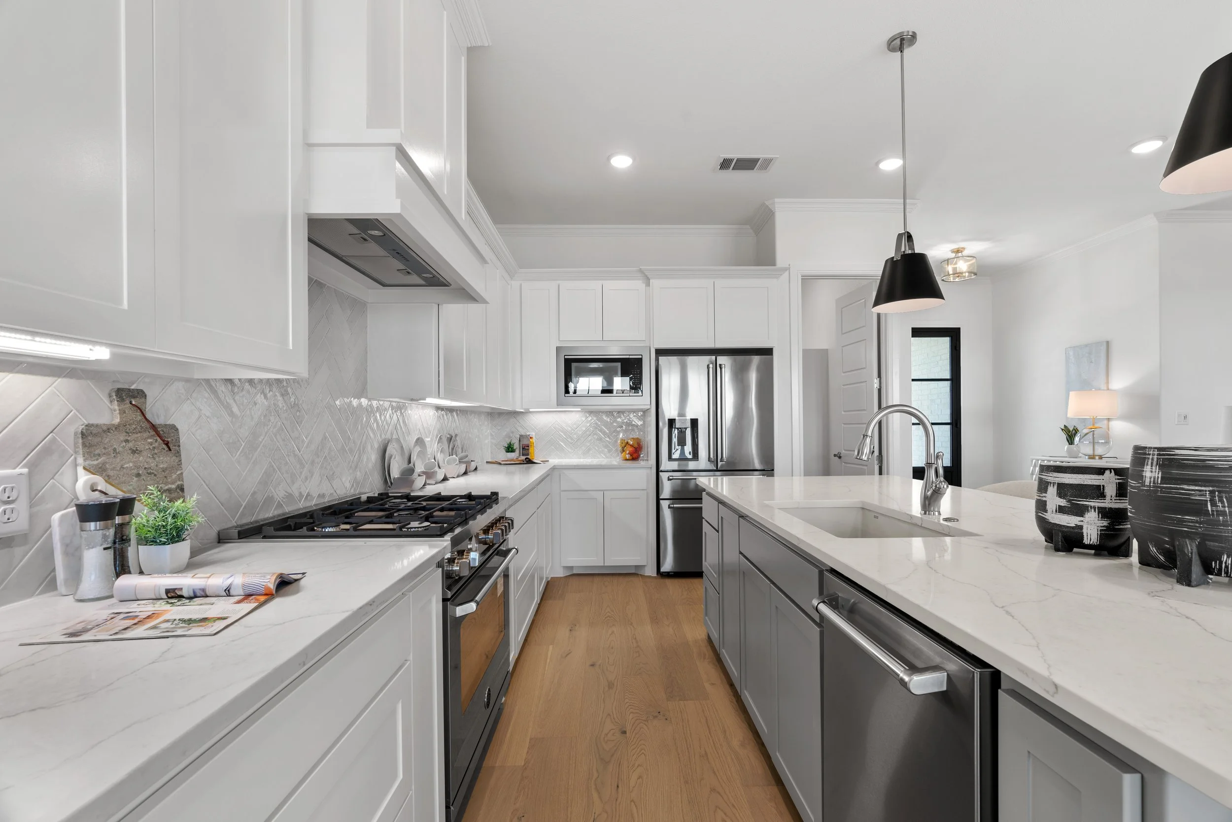 Modern kitchen with white cabinets, stainless steel appliances, and a marble island with black pendant lights.