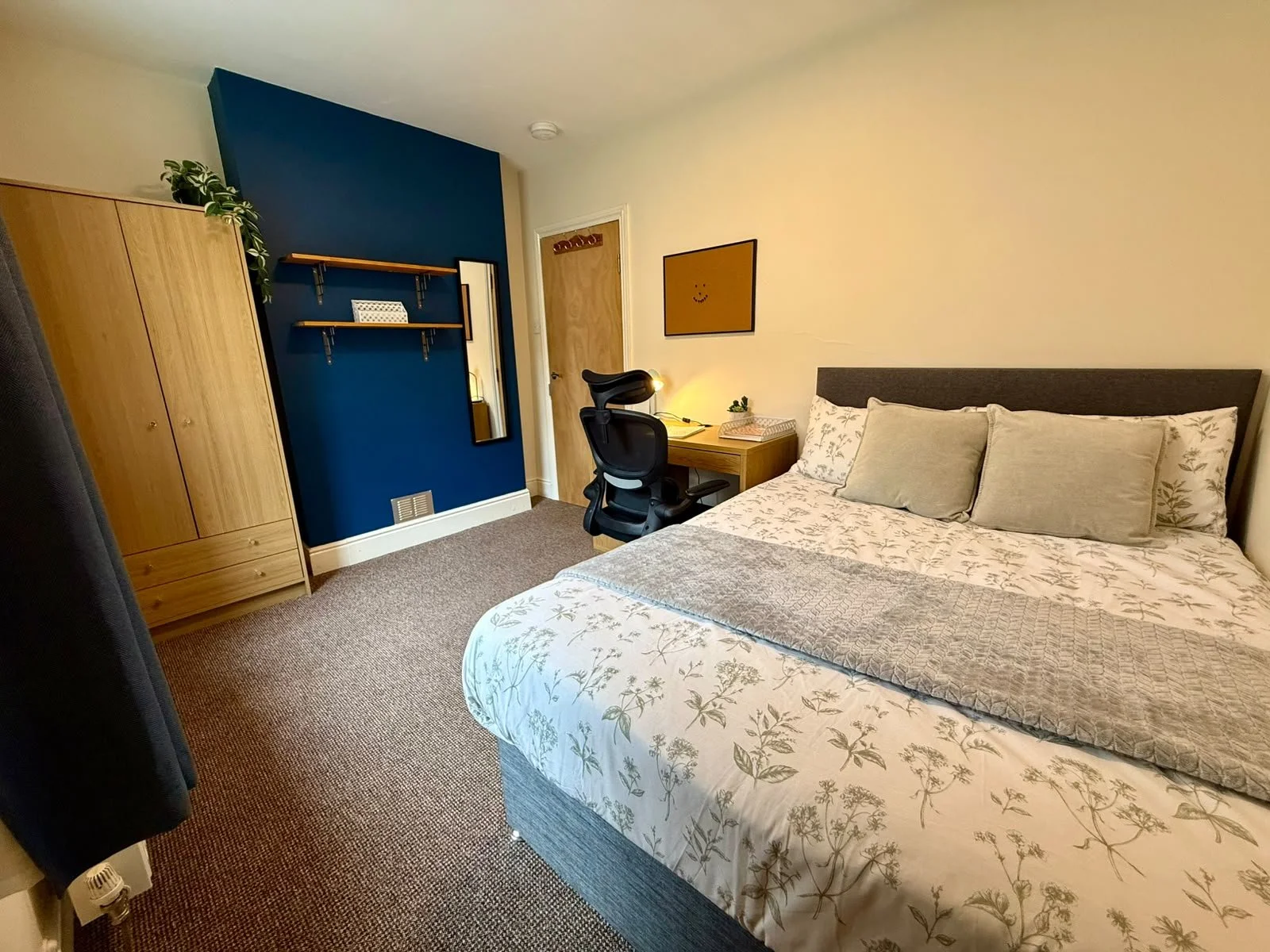 A bedroom with a bed, desk, chair, wardrobe, and a blue accent wall.