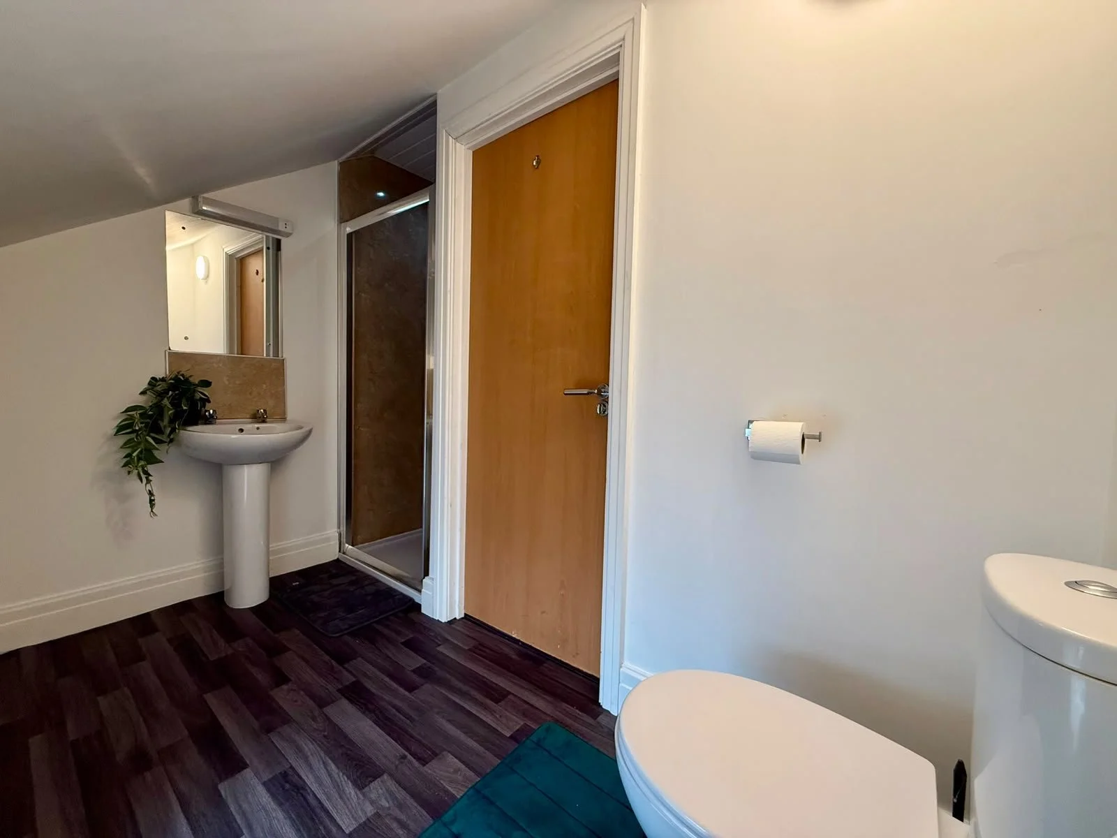 Bathroom with a white sink, a mirror, a wooden door, a toilet paper holder, and a toilet, with dark wood flooring.