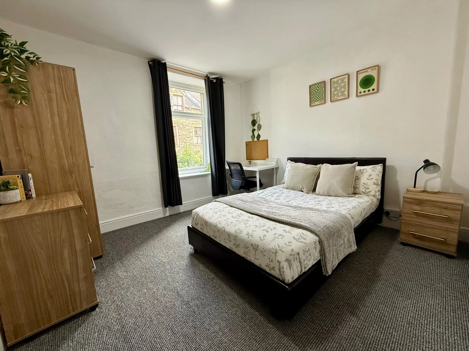 A bedroom with a bed, nightstand, desk, bookshelf, window, and wall art.