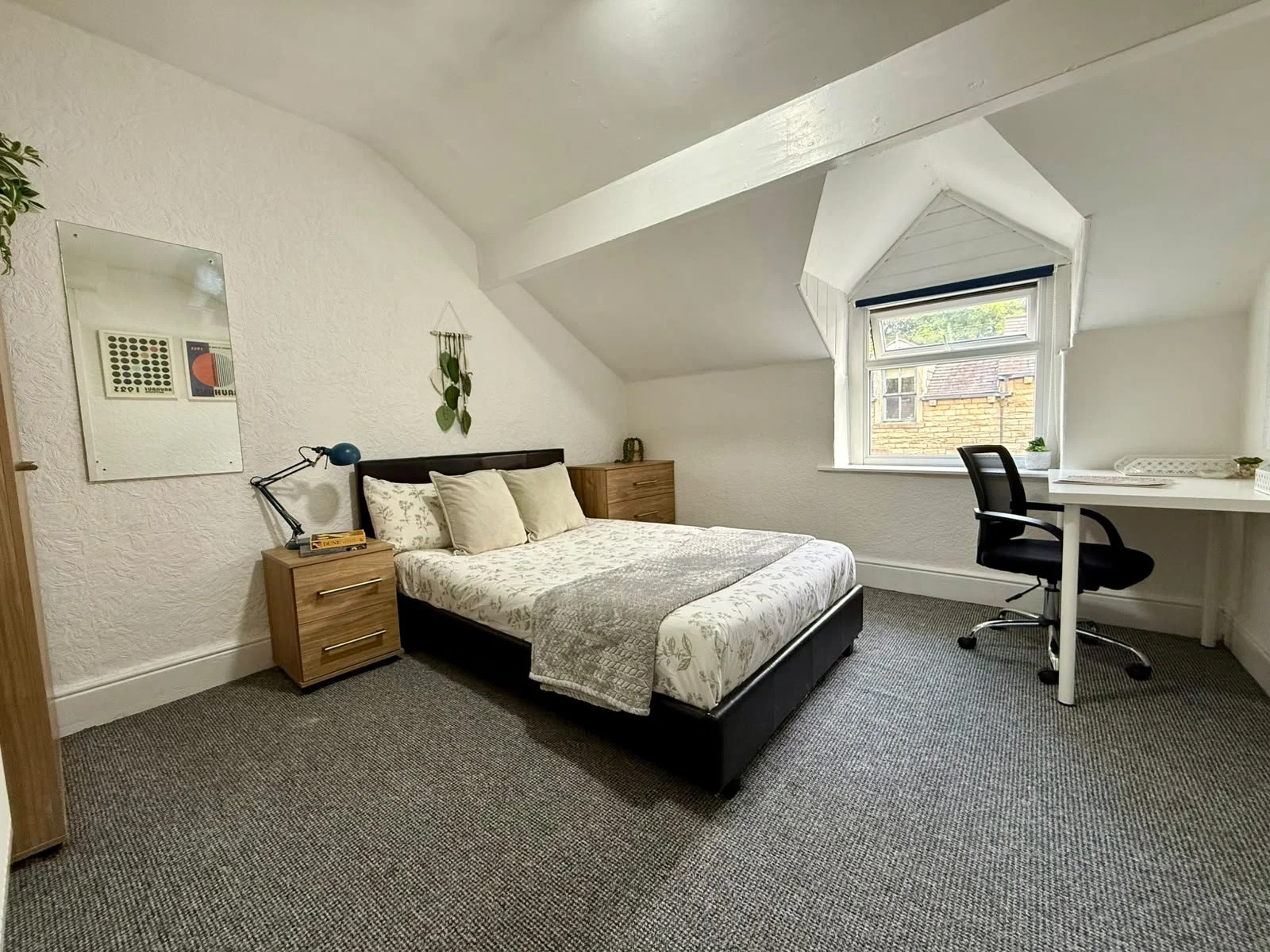 A bedroom with a bed, two wooden nightstands, a window, a desk, and a swivel chair.