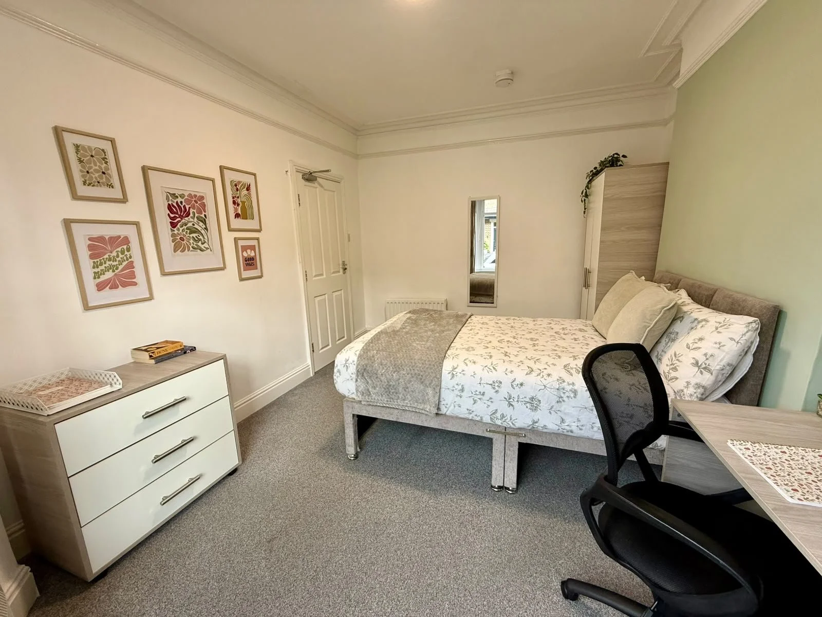 A bedroom with a bed, dresser, wall art, a mirror, a wardrobe, and a desk with a chair.