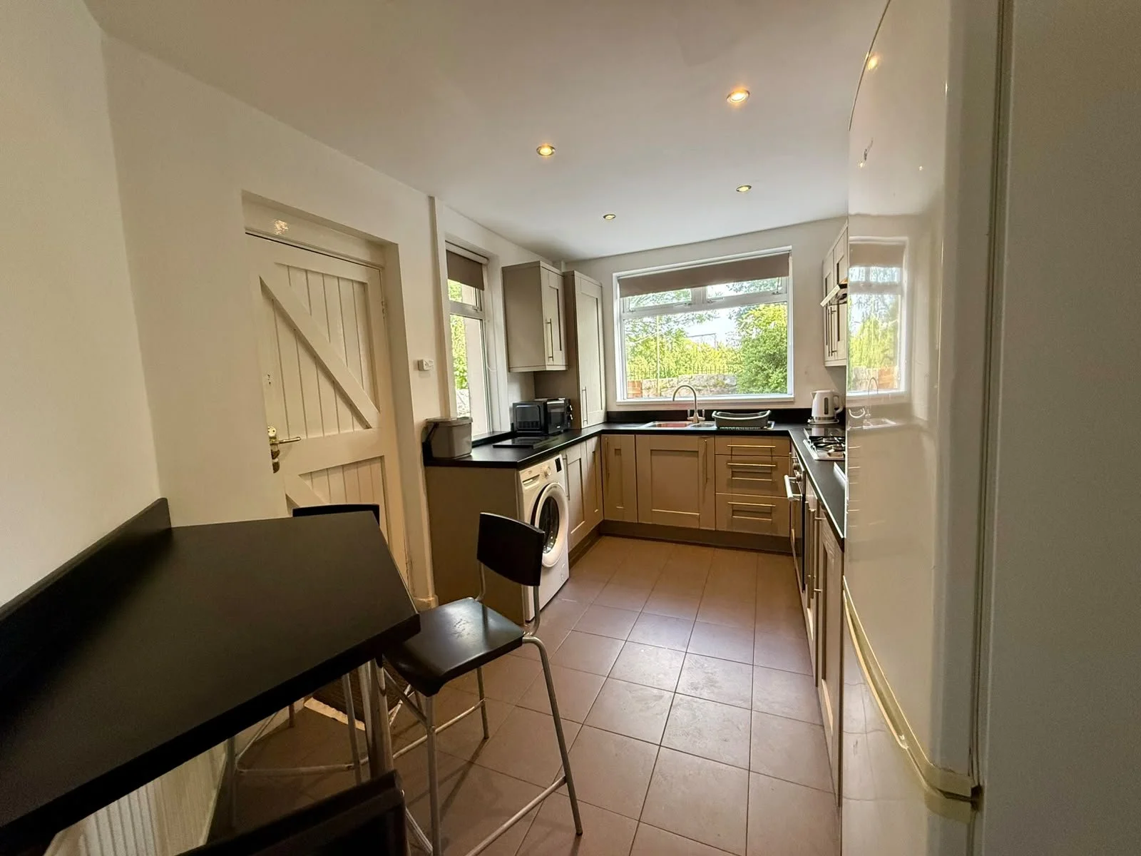 Kitchen with beige cabinets, black countertop, washing machine, microwave, toaster, kettle, and window showing greenery outside.