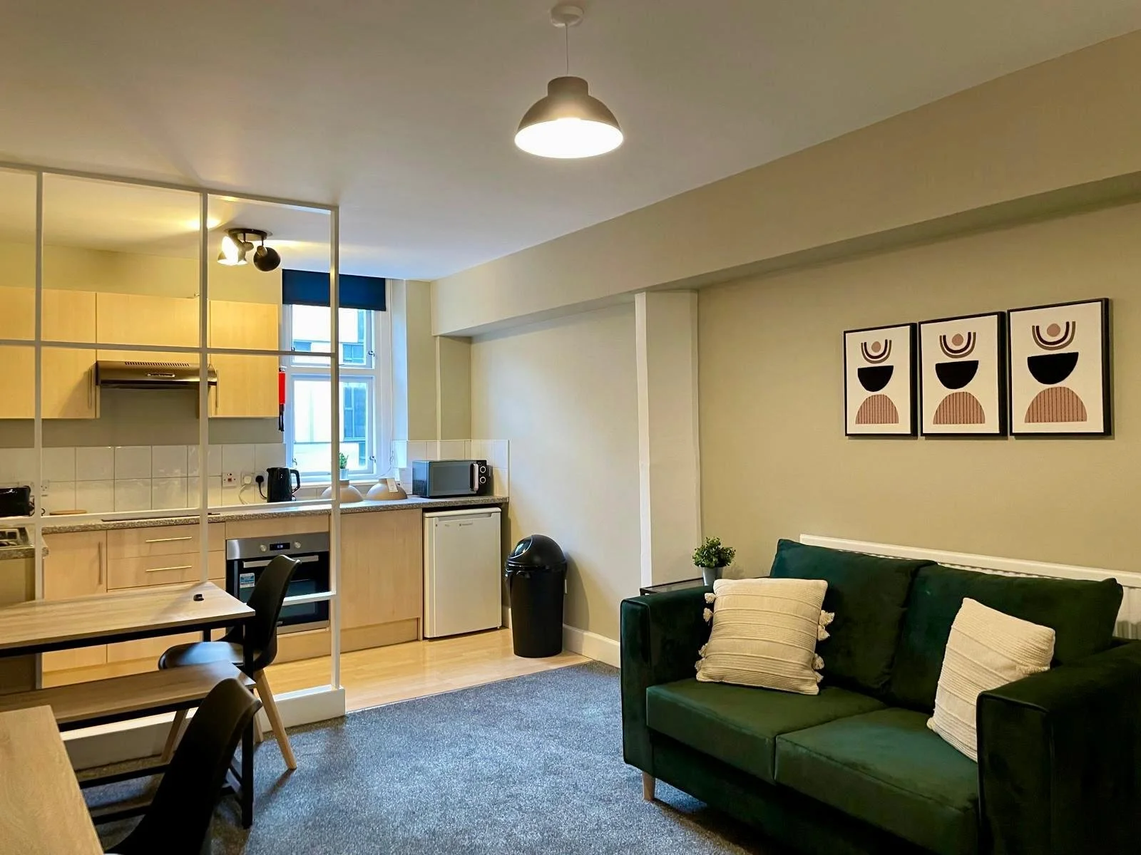 Inside a modern studio apartment with a green sofa, a bed, and wooden furniture, decorated with abstract wall art and potted plants.