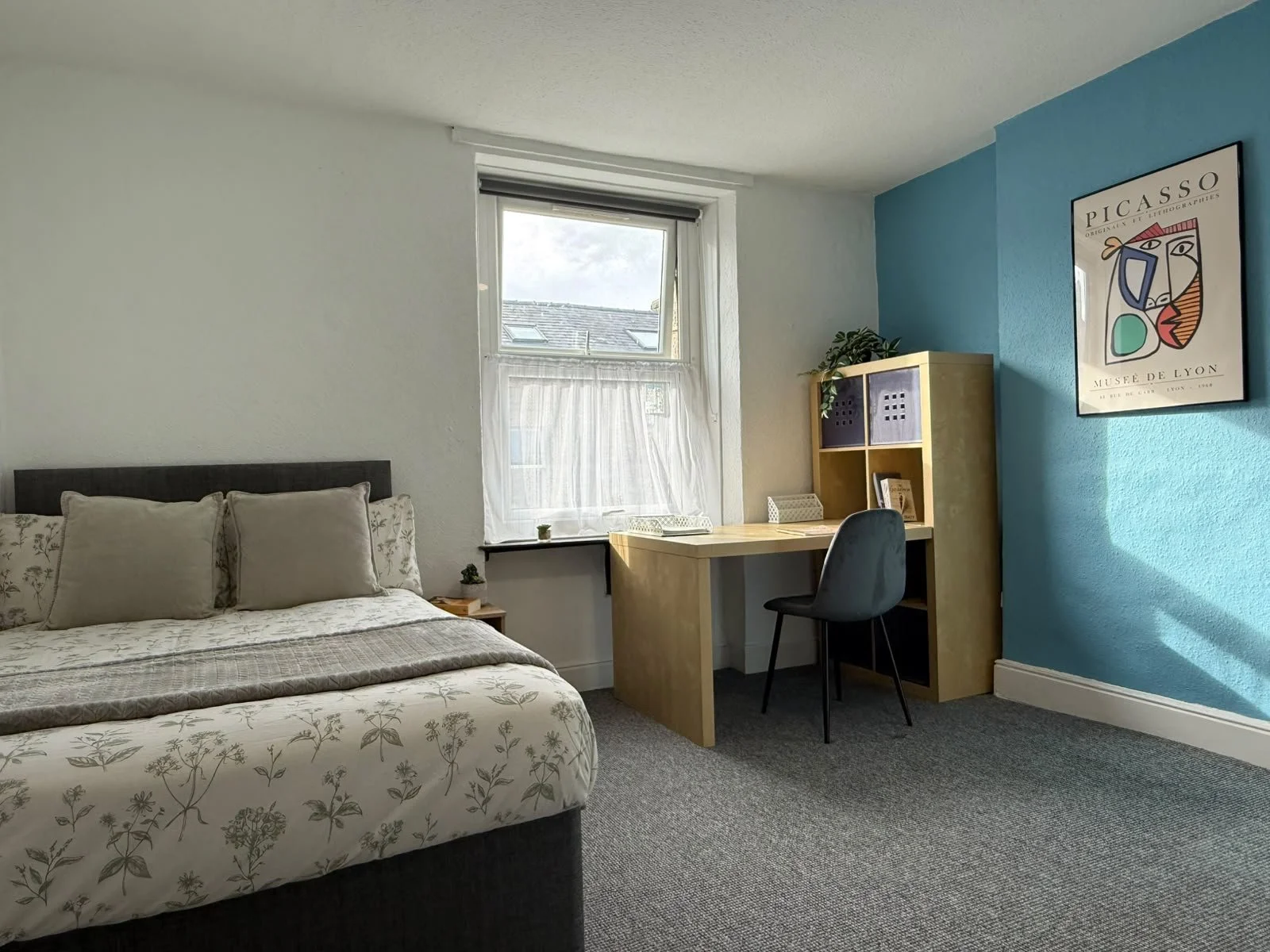 Bedroom with bed, window, desk, chair, bookshelf, and poster on blue wall.