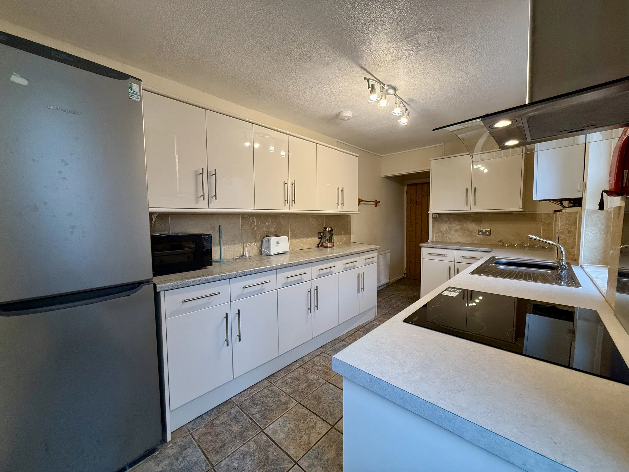 Modern kitchen with white cabinets, gray countertops, stainless steel appliances, and tiled floor. Features a refrigerator, microwave, toaster, and electric stovetop.