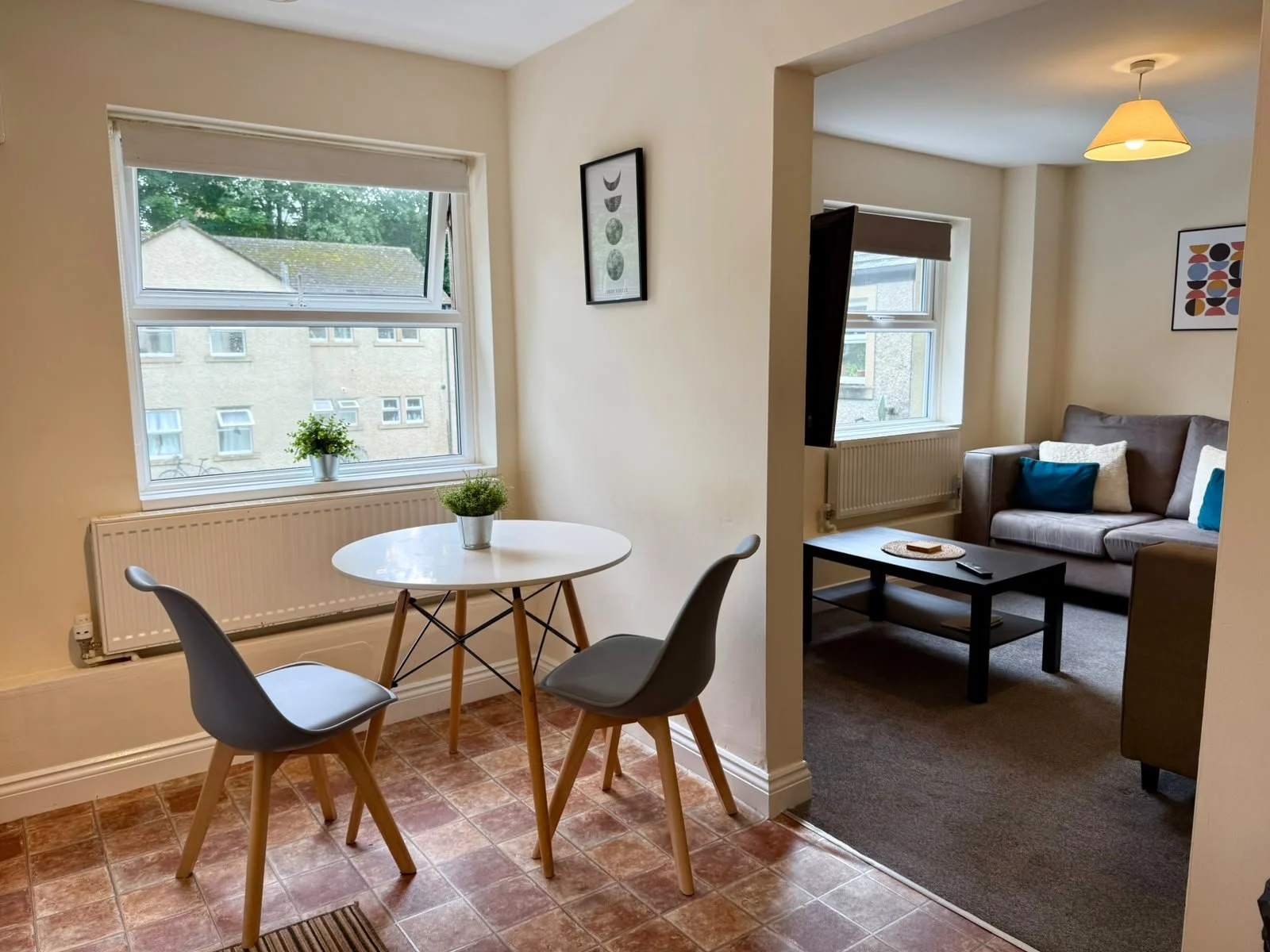 Modern kitchen with white cabinets, a washing machine, microwave, toaster, rice cooker, and a small table with two chairs by a large window.