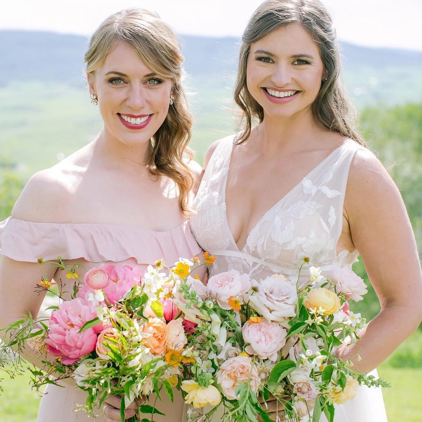 Two women smiling outdoors holding a large bouquet of colorful flowers.