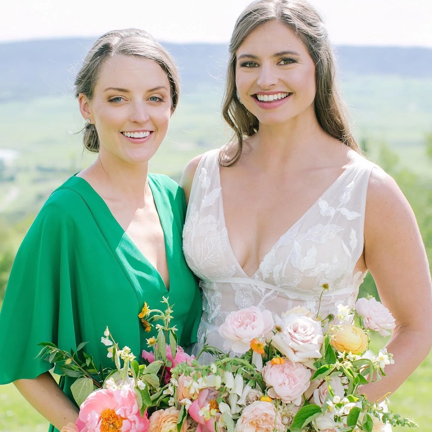 Two women standing outdoors holding a bouquet of flowers, smiling at the camera.