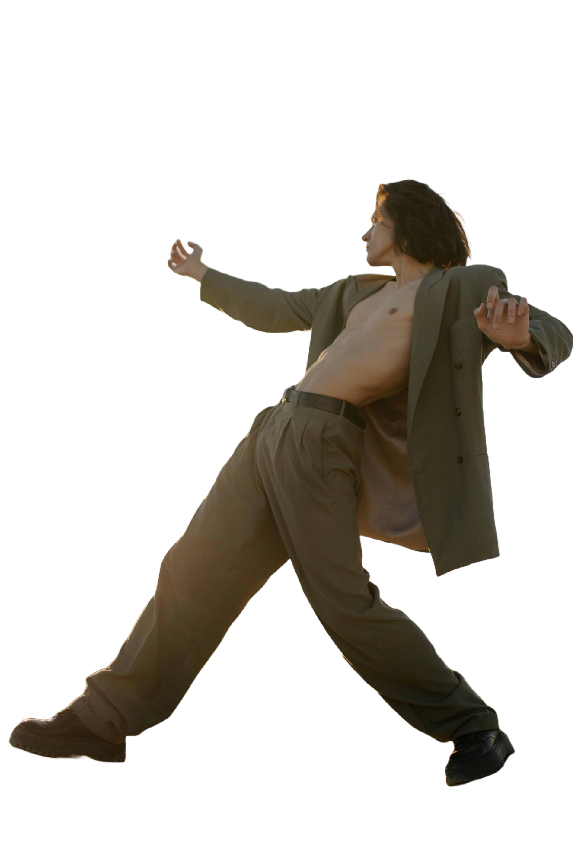 A man with long hair, dressed in a suit with no shirt underneath, is striking a dynamic pose with one arm extended outward and the other bent. He appears to be leaning back dramatically with one leg bent and the other extended, set against a plain background.