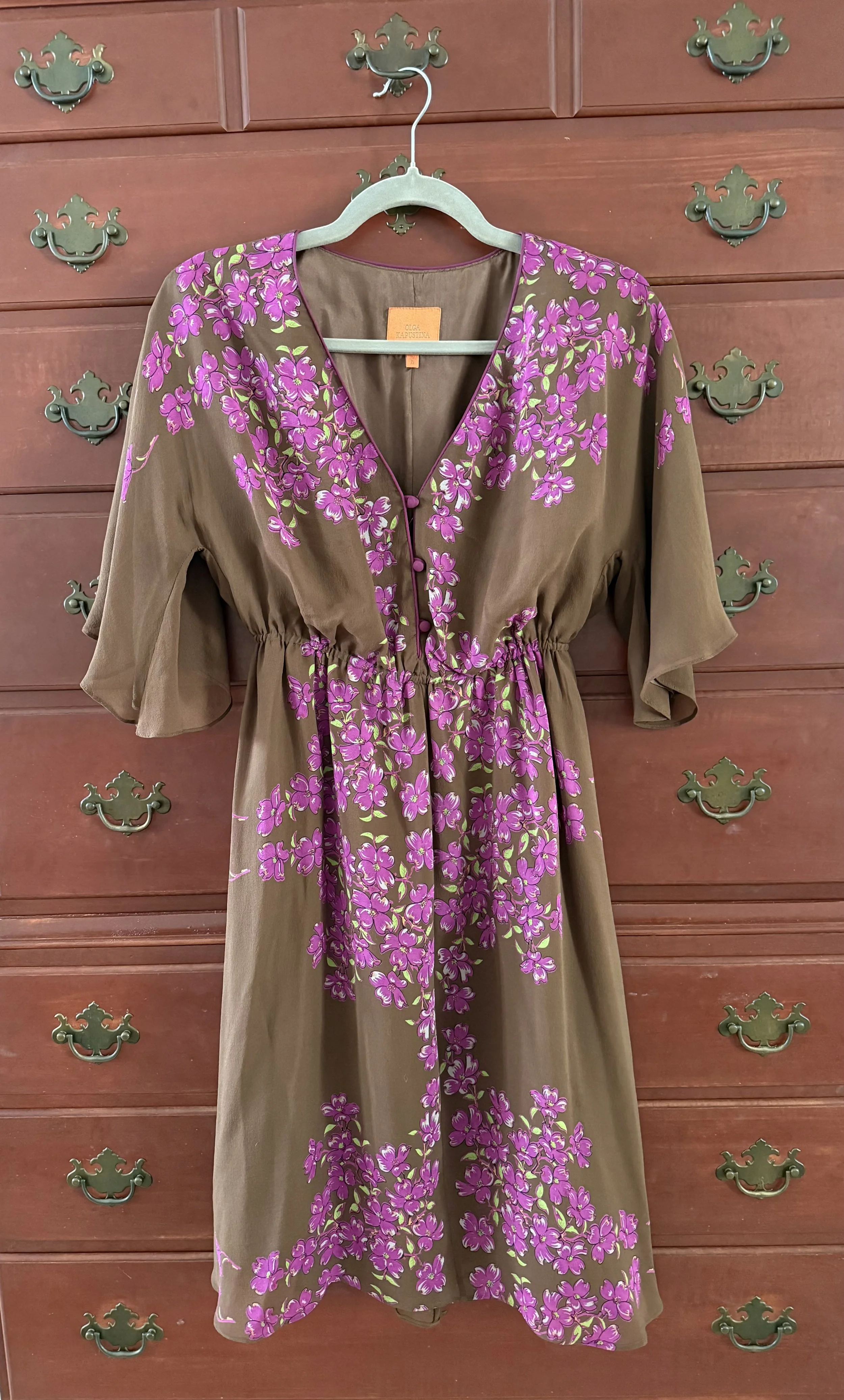 Brown dress with bright pink floral print, short flutter sleeves, and button front, hanging on a wooden dresser.