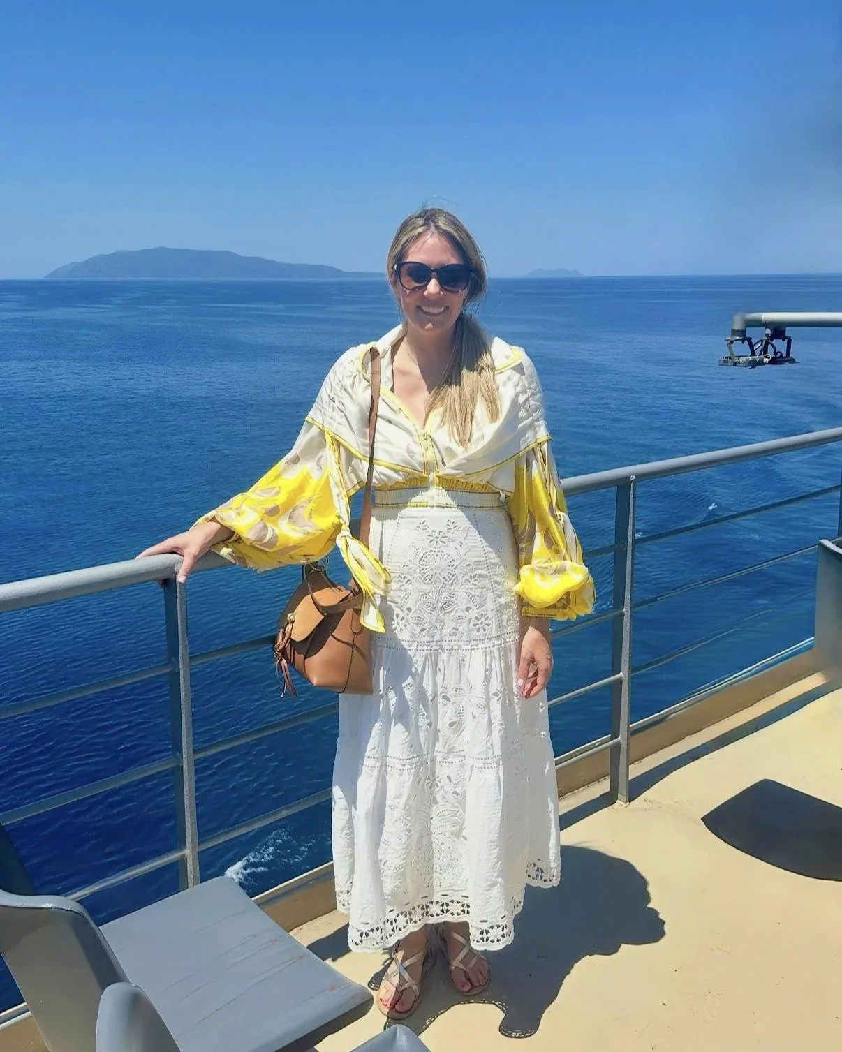 Woman in a white summer dress and yellow blouse on a ferry with ocean scenery.