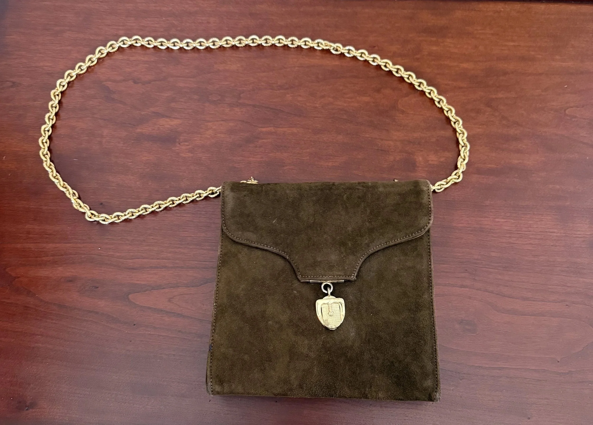 Vintage brown suede handbag with gold chain strap and gold clasp, displayed on a wooden surface.