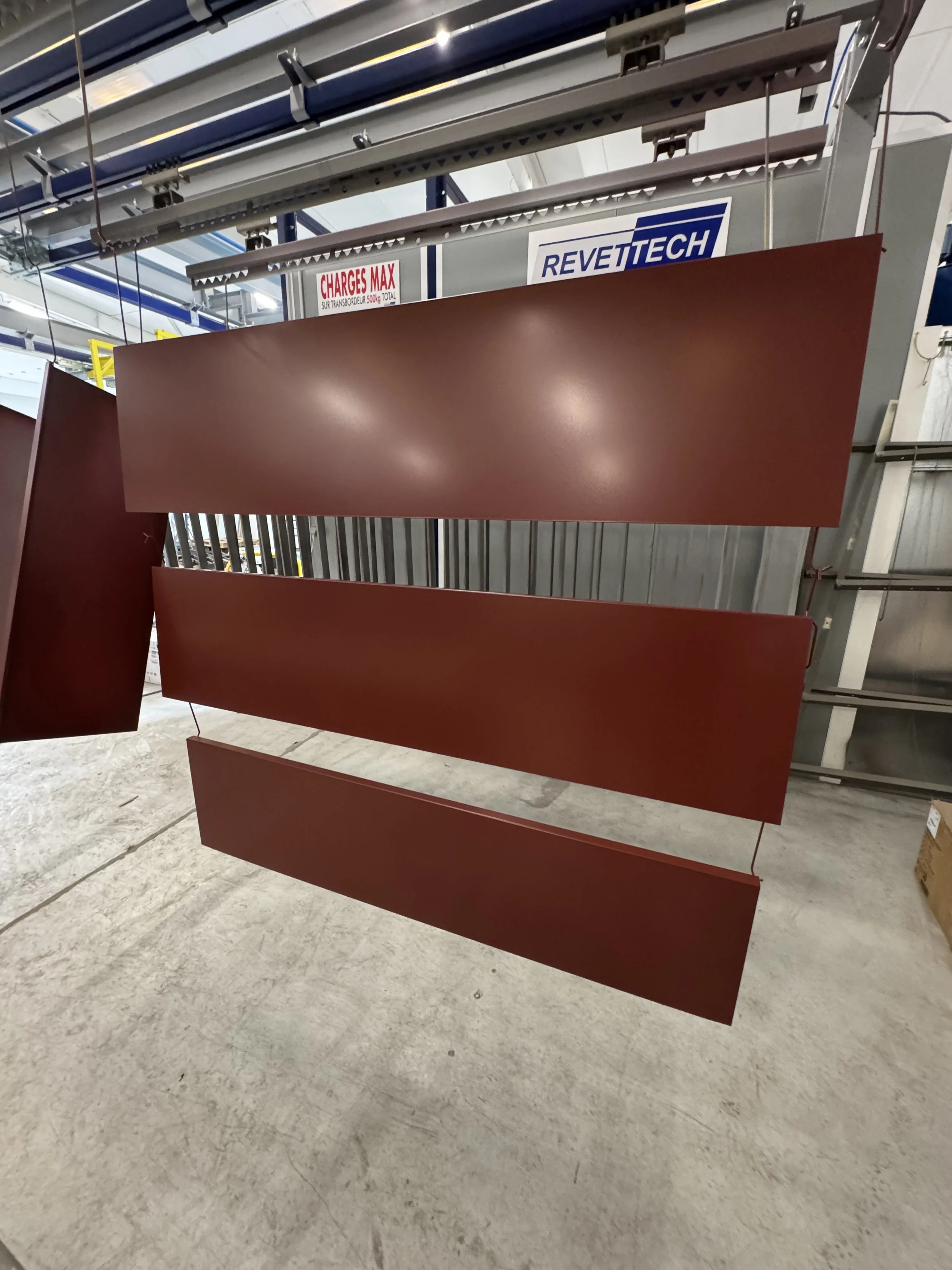 Plaques en métal doré et martelé suspendues dans un espace industriel, avec des panneaux signalétiques en arrière-plan