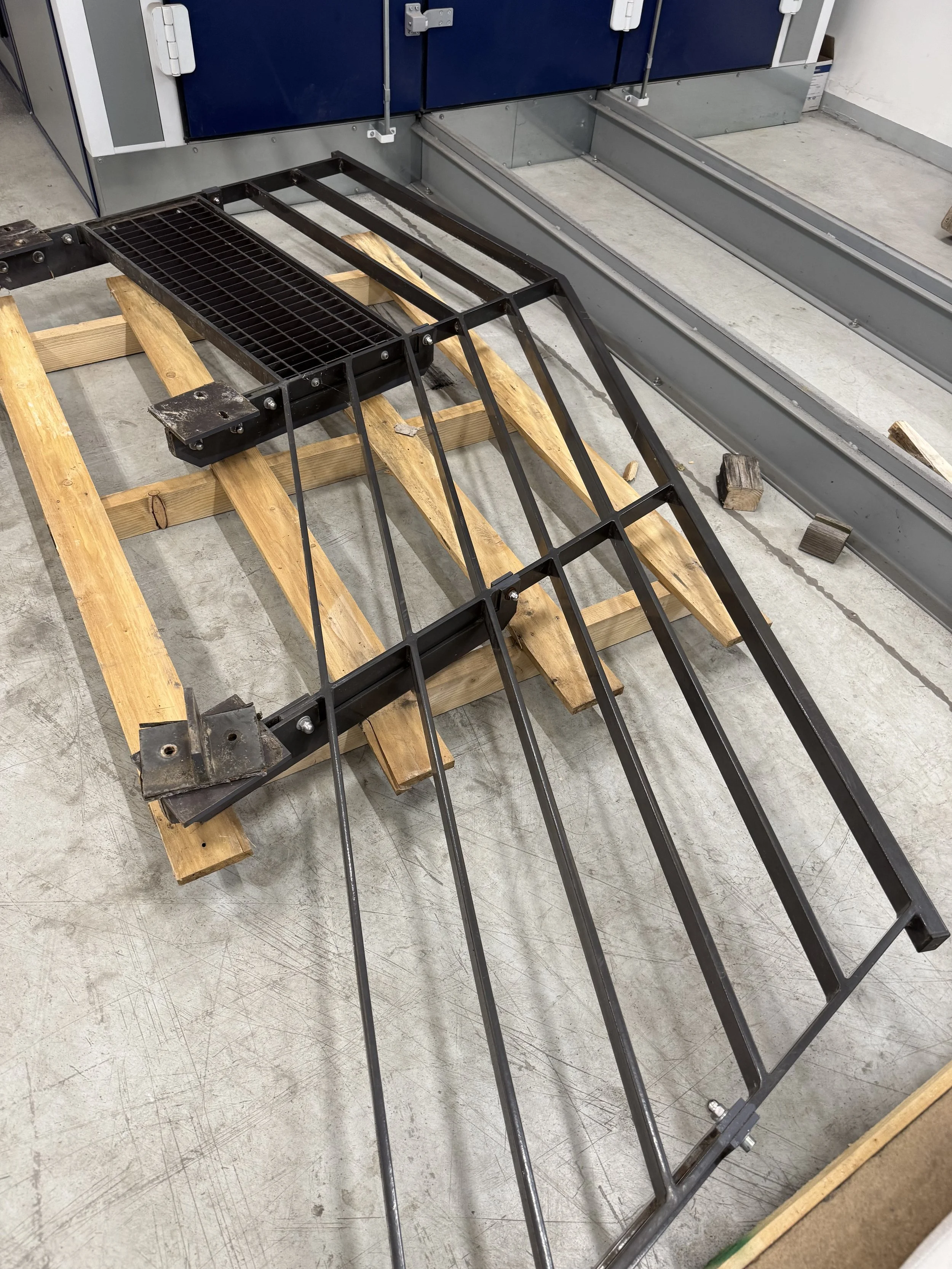 Structure métallique noire assemblée sur une base en bois, probablement une partie d'un meuble ou d'une étagère, située dans un atelier.