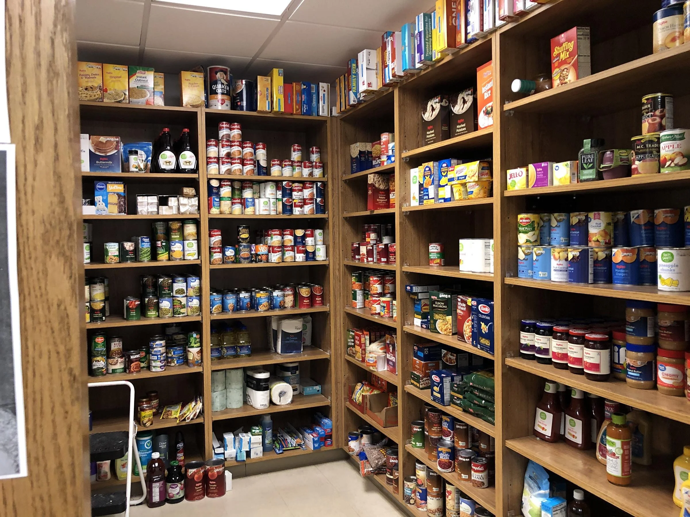 A pantry with wooden shelves filled with canned goods, boxed foods, condiments, and bottles, organized neatly.