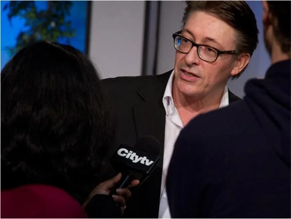 A man in glasses and a suit being interviewed by a person holding a Citytv microphone.