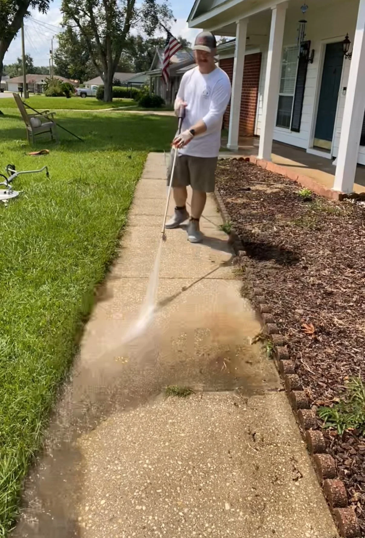 Person power washing a concrete sidewalk in front of a house on a sunny day.