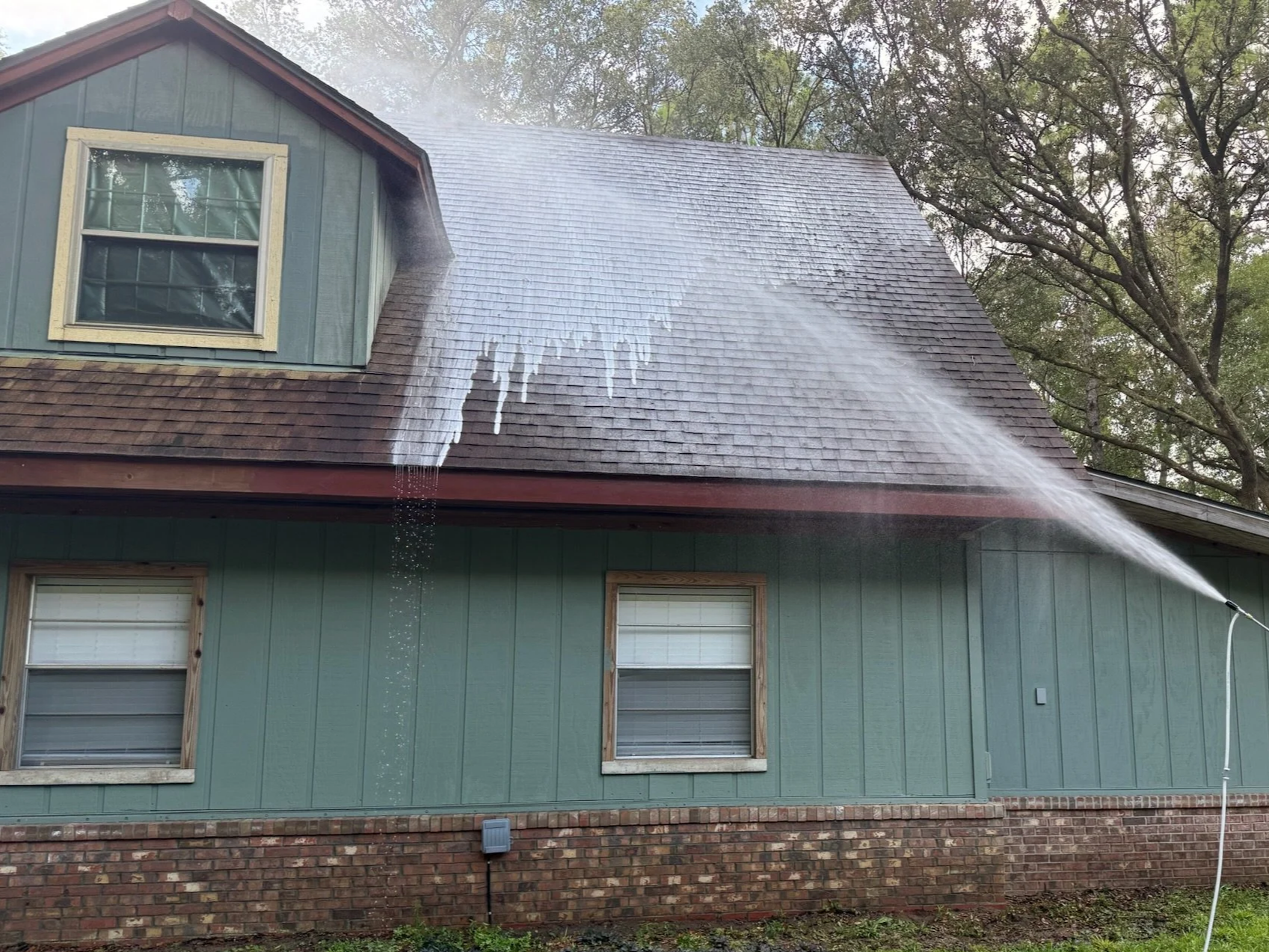 A house being sprayed with water  and chemicals to clean or cool the roof. This is soft washing a roof.