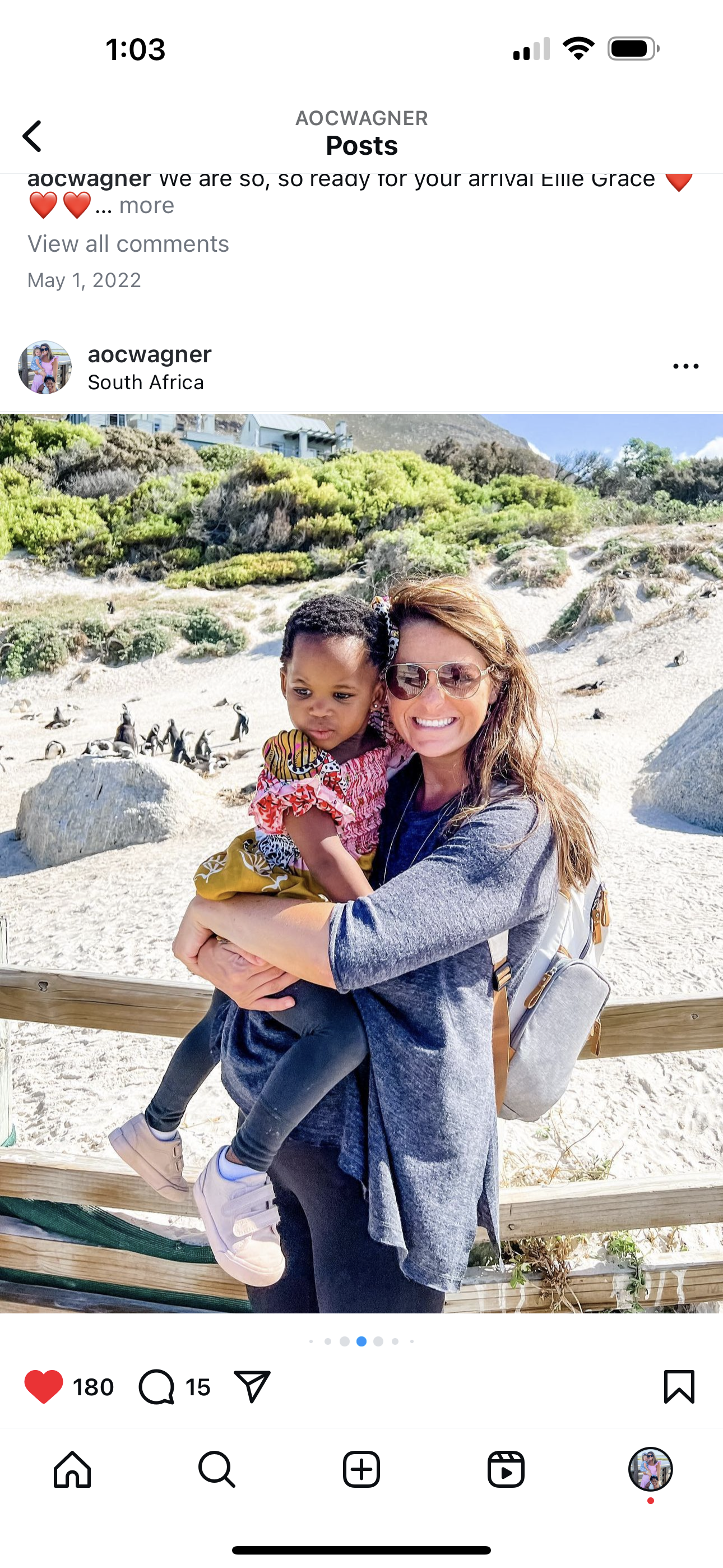 Just Another Wagner Adventure | A woman with sunglasses holding a young girl in front of a beach with penguins and rocky dunes in the background. Boulder's Beach in South Africa.