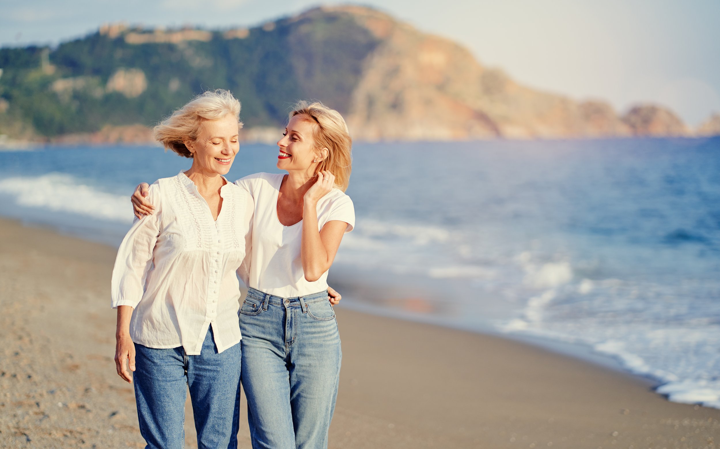 other and adult daughter walking together on the beach to stay active and maintain strength and independence throughout the aging process.