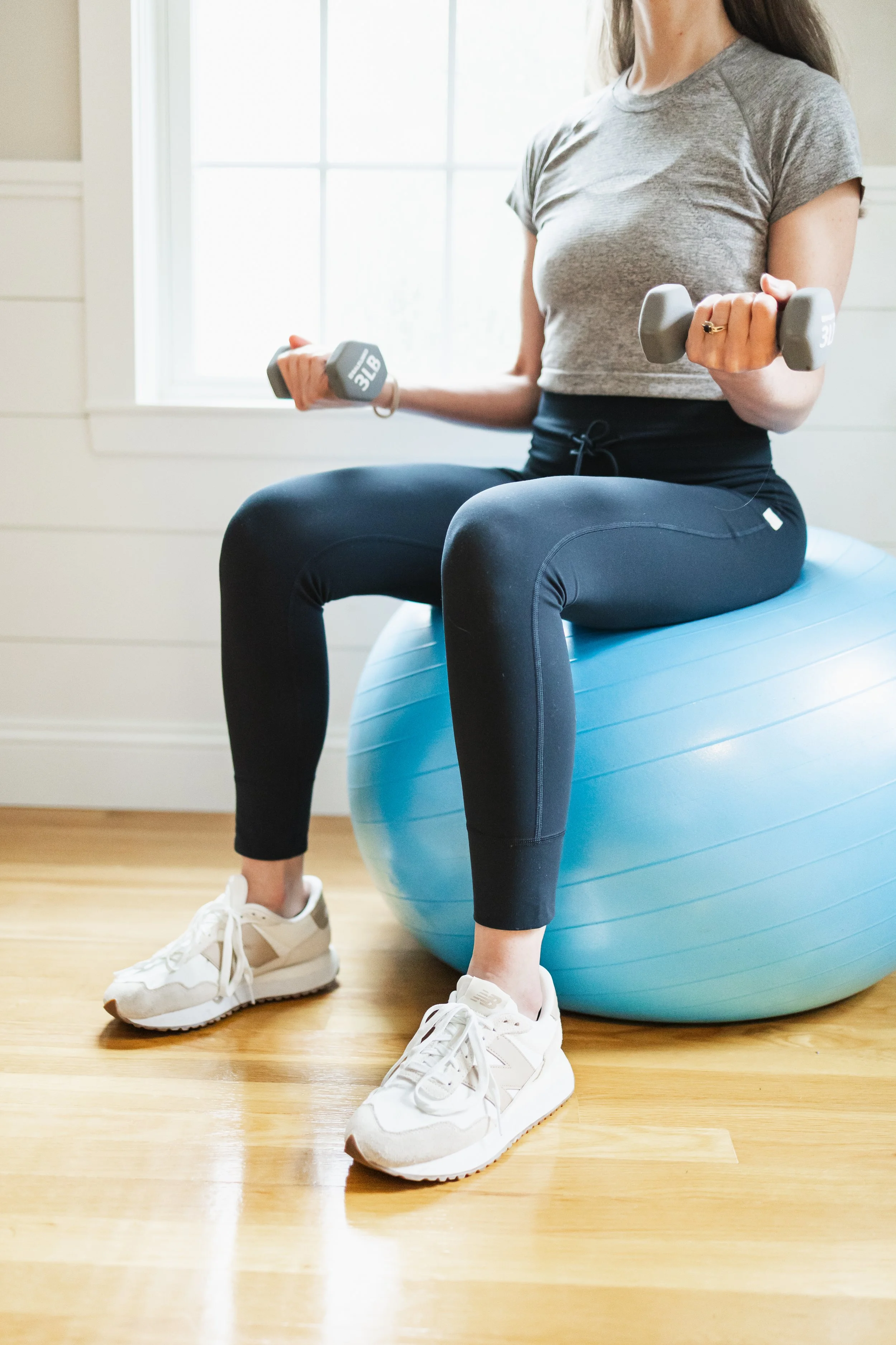 Woman seated on an exercise ball holding dumbbells.