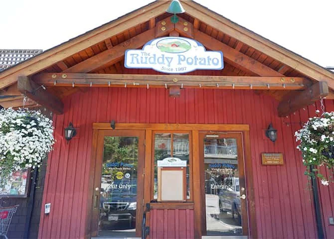 Front view of The Reddy Potato restaurant with red exterior, wooden accents, flower baskets on each side, and hanging signs displaying the name and entrance.