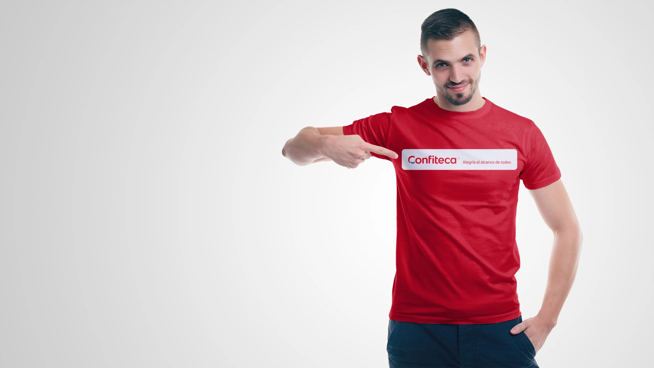Hombre joven con camiseta roja de Confiteca señalando el logotipo y eslogan “Alegría al alcance de todos”, sobre fondo claro. Imagen corporativa que refleja orgullo de pertenencia, identidad de marca y actitud positiva en el entorno laboral.