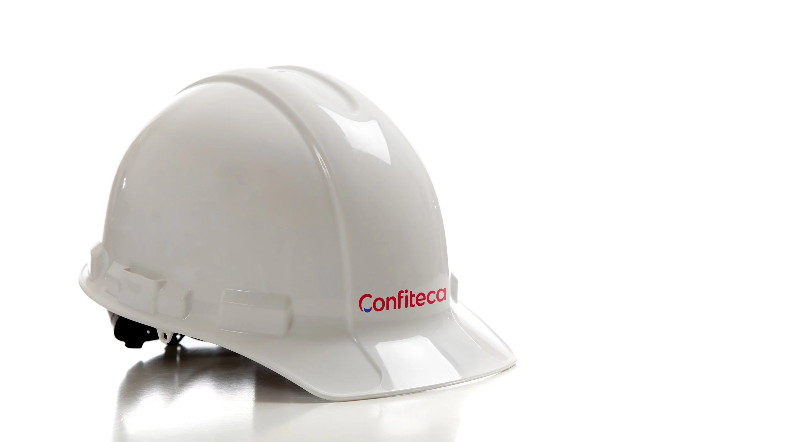 Casco de seguridad blanco con logotipo de Confiteca impreso en el frente, sobre fondo blanco. Equipo de protección industrial que representa el compromiso de la marca con la seguridad laboral y las buenas prácticas en entornos de producción.