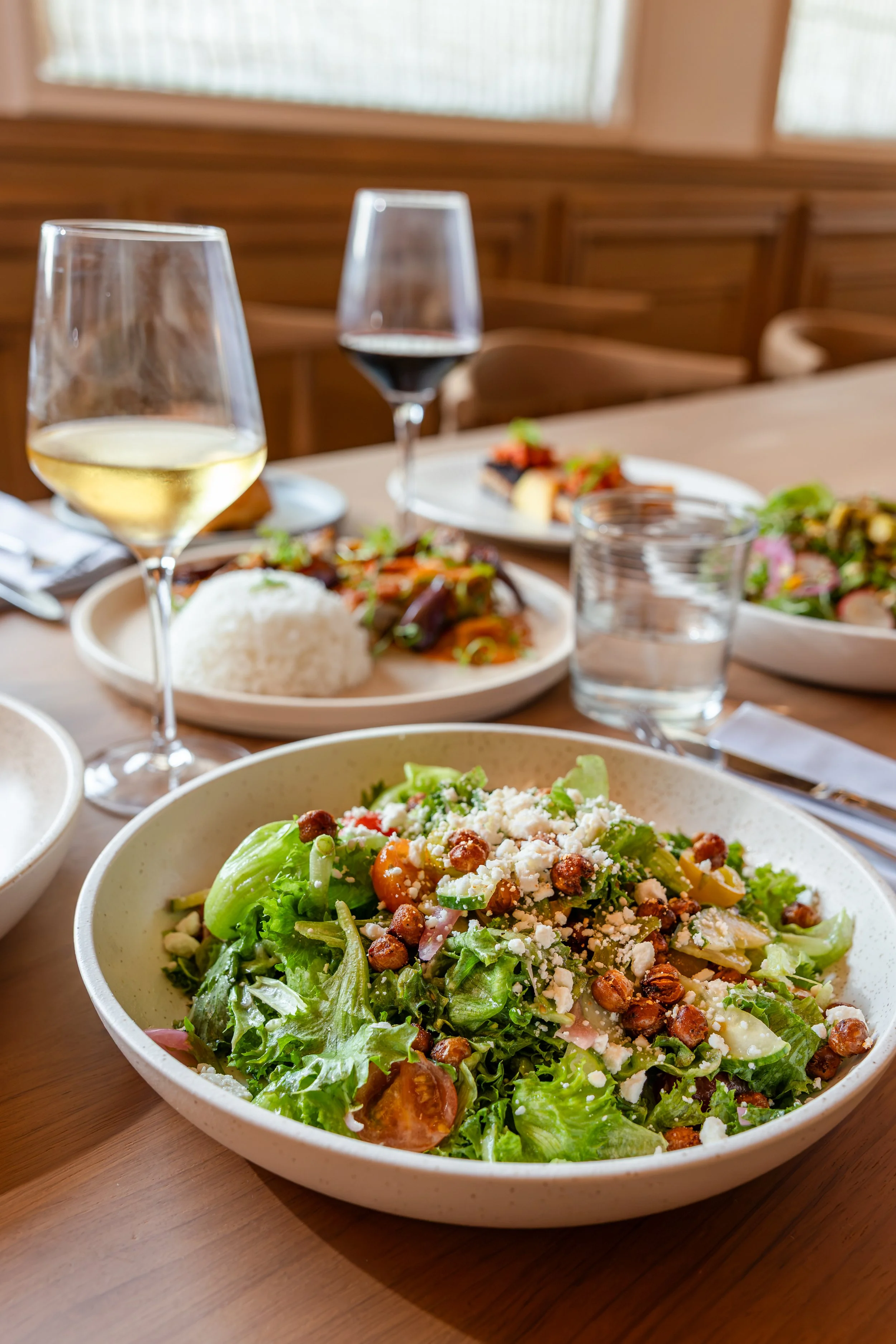 A large bowl of salad with lettuce, cherry tomatoes, shredded cheese, and crispy chickpeas on a wooden table.