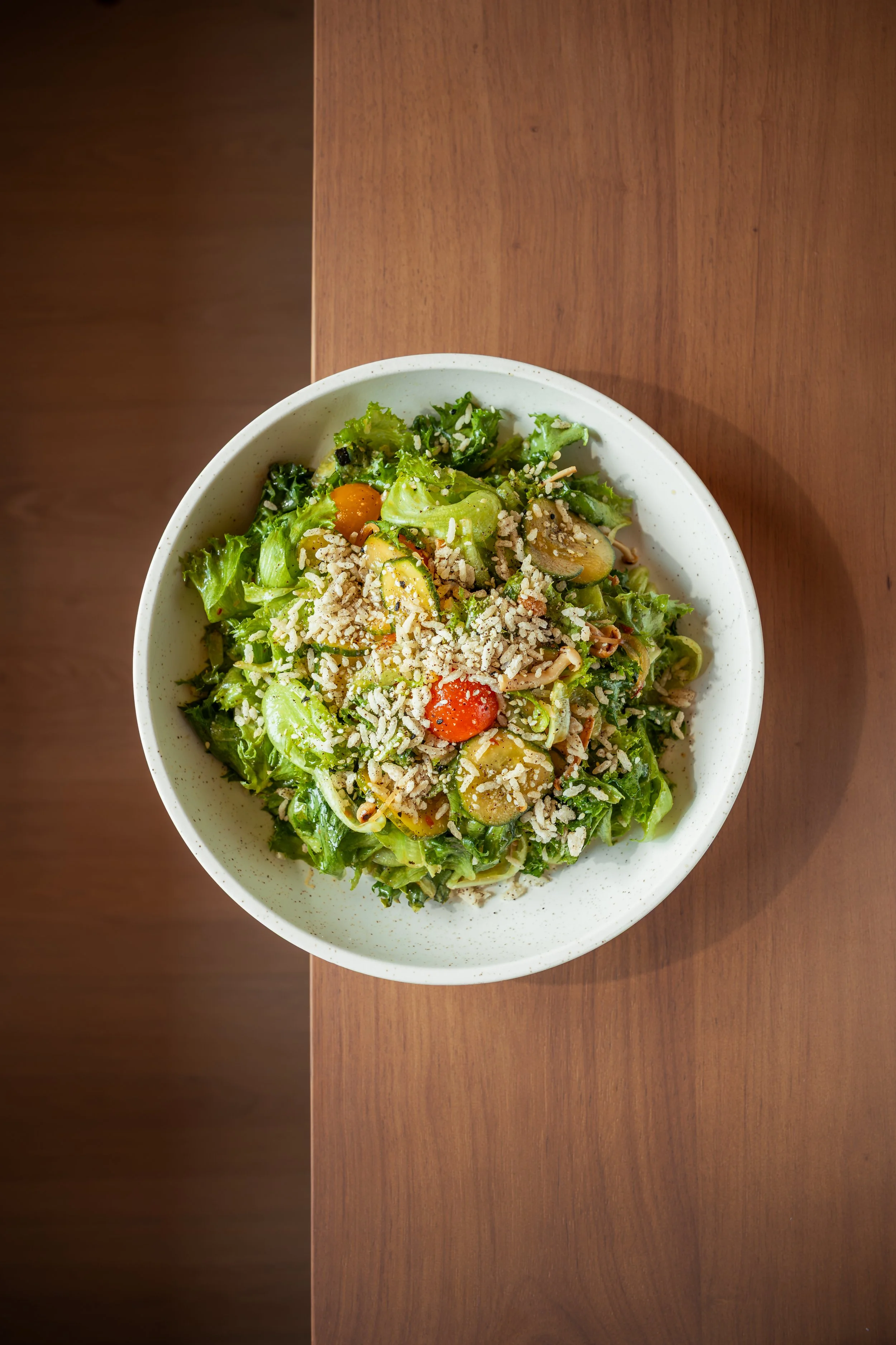 A bowl of salad with lettuce, cherry tomatoes, cucumbers, and shredded cheese on a wooden table.