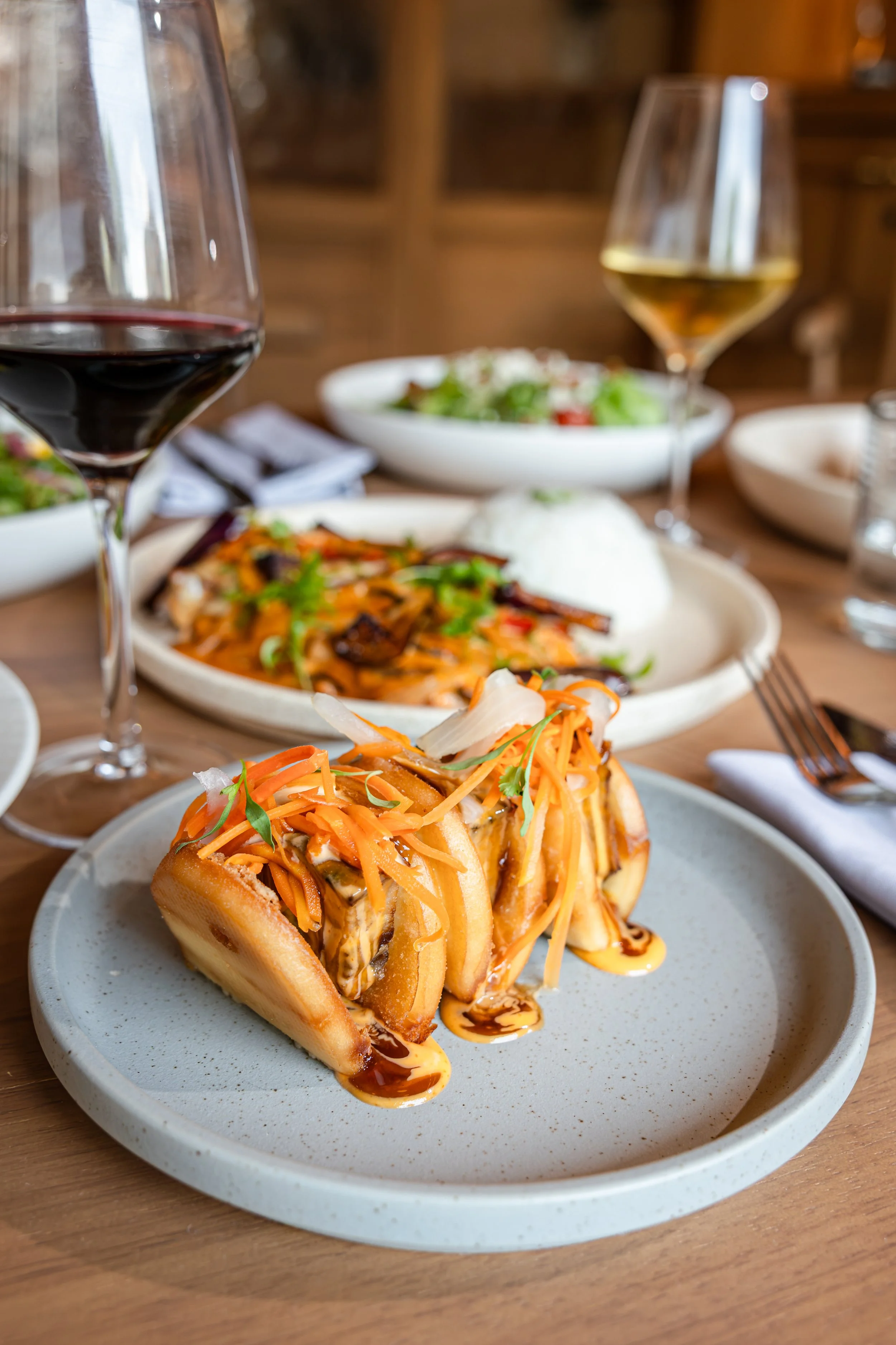 Hot dog topped with shredded carrots, herbs, and drizzle of sauce on a ceramic plate.