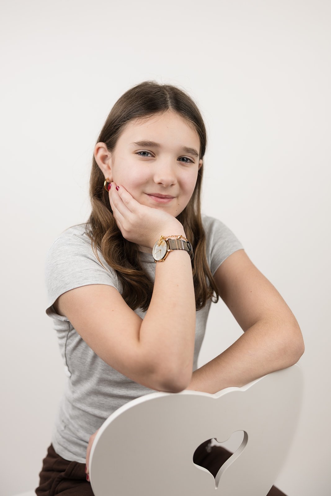 Junge Frau mit braunen Haaren, grauem T-Shirt, trägt eine Armbanduhr und eine Ohrring, sitzt an einem weißen Tisch mit Apple-Logo, vor weißem Hintergrund.