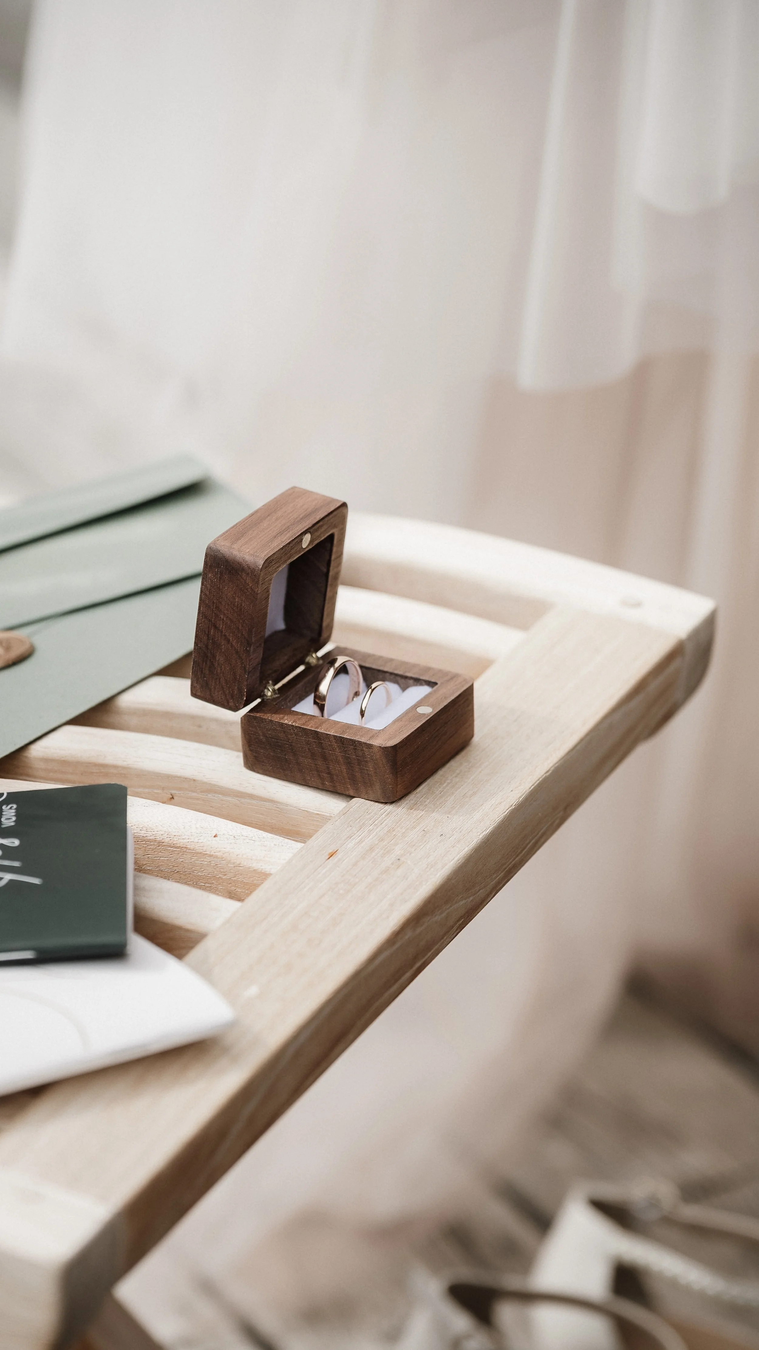 Ein offenes Holzkästchen mit goldenen Ringen auf einer Holzbank.