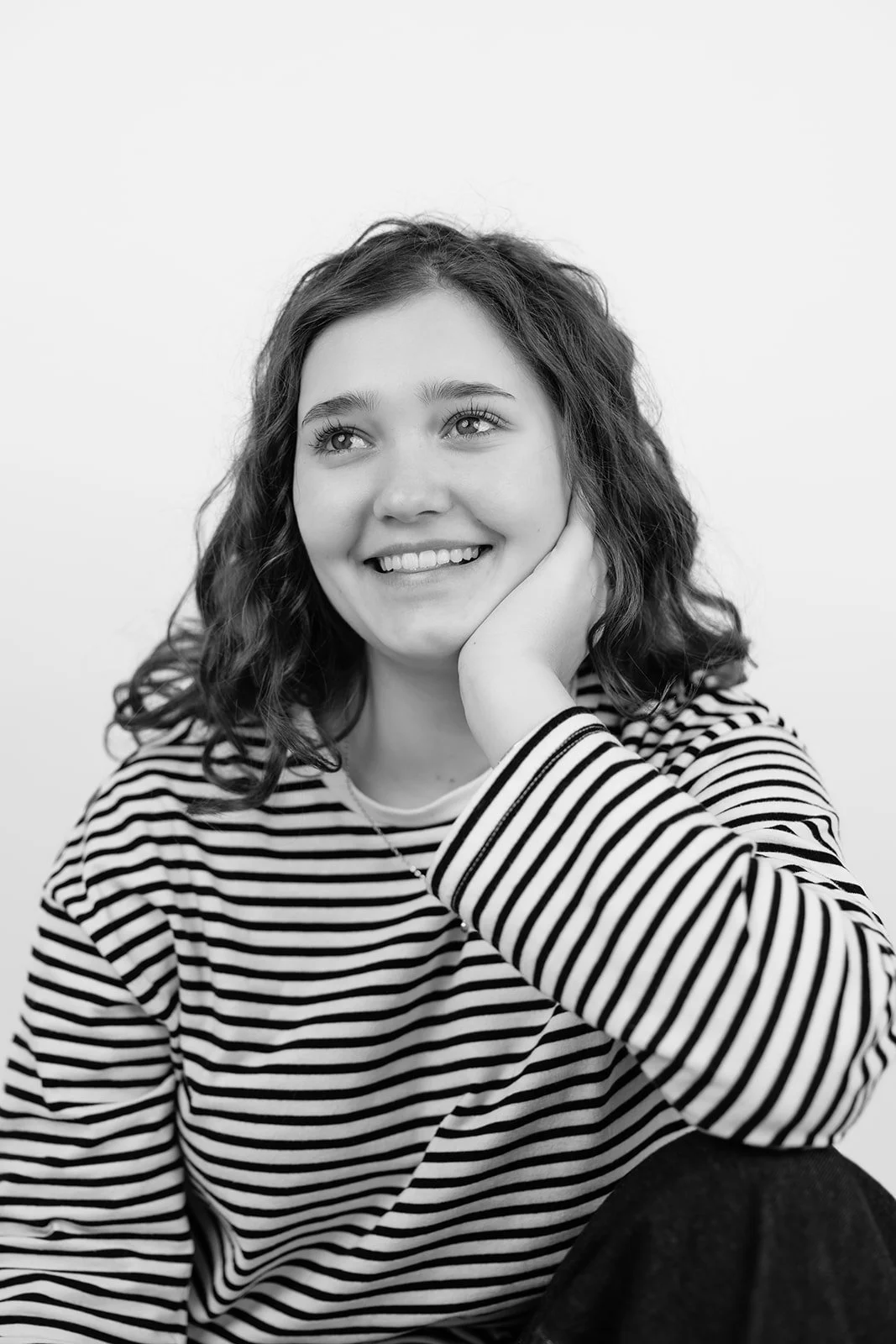 Lächelnde junge Frau mit lockigem Haar in einem Streifen-Shirt, die stilvoll lächelt